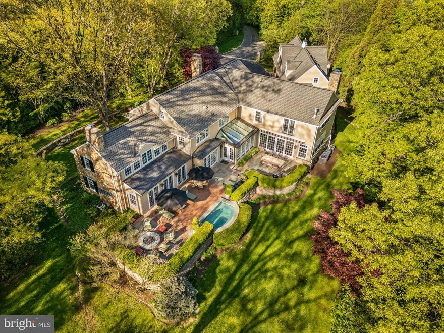 Discover a timeless blend of Main Line elegance and modern luxury at 1333 Beaumont Road in Gladwyne, a beautifully expanded stone Colonial set on 3.26 private, gated acres along one of the area’s most coveted streets. Built by the original owner, Bob Warner, who served as the contractor for most, if not all, of Beaumont Drive, the home reflects a deep understanding of fine craftsmanship and timeless design.

A sweeping driveway leads to the front entrance, flanked by stone piers and lush landscaping. The stone facade, reminiscent of historic Main Line estates, seamlessly integrates with its surroundings, creating a sense of permanence and legacy.

Inside, the home is filled with natural light from an exceptional number of generous windows, illuminating rich hardwood floors, traditional moldings, and thoughtful design throughout. The main level offers an ideal layout for modern living and entertaining. A transverse entry foyer introduces the home’s open, flowing design, leading to a series of gracious rooms perfect for both large gatherings and quiet retreats.

The expansive living room, with windows on three exposures, features a fireplace and three sets of French doors that open to the terrace, creating a seamless connection between indoor and outdoor living. Nearby, a handsome library with a fireplace and custom built-in cabinetry offers a quiet space for work or reading. The formal dining room, ideal for both intimate dinners and larger celebrations, features glass doors that open to a brick terrace, extending the entertaining space into the gardens. The main level also includes a well-appointed home office with built-in cabinetry and a custom desk, providing a dedicated workspace with a refined, professional atmosphere.

At the heart of the home is the gourmet kitchen, equipped with premium stainless appliances, a large center island with counter seating, and an adjacent breakfast room with atrium-style windows overlooking the picturesque grounds. Just beyond, the family room, with decorative ceiling beams and a floor-to-ceiling stone fireplace, opens through glass doors to a flagstone terrace, perfect for outdoor gatherings. A separate catering kitchen, outfitted with double Sub-Zero refrigerators, extensive cabinetry, and a second sink, adds convenience for large gatherings or intimate family dinners.

The second level features five generously sized bedrooms, each with its own private bath, including a remarkable primary suite with a gas fireplace, French doors to a Juliet balcony, and a luxurious bathroom with a glass-enclosed steam shower, whirlpool tub, double vanities, and a dedicated makeup area. This level also includes a dedicated massage and yoga room, offering a tranquil retreat for wellness and relaxation.

An impressive addition includes a four-car garage with a private, apartment-like suite above – ideal for guests, in-laws, or a live-in caretaker. Accessible via a separate staircase, this suite includes a living room, kitchenette, dining area, bedroom, and full bath, providing complete independence from the main house.

The grounds are truly magical, with stately trees, mature landscaping, and breathtaking views that change with the seasons. Outdoor living spaces include flagstone and brick terraces, a built-in circular natural-gas firepit, an in-ground whirlpool spa, a serene water feature, a garden shed, and an outdoor shower, creating an enchanting setting for both quiet reflection and lively gatherings.

With its private yet convenient location, extensive outdoor living spaces, and thoughtful, high-quality renovations, 1333 Beaumont Road is a truly remarkable residence for those seeking an exceptional Main Line lifestyle.