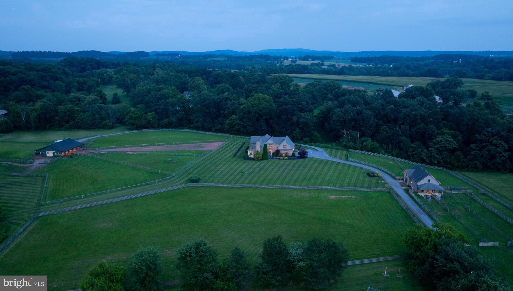 Welcome to 380 Meadow Lane, a stunning 31.47± acre estate nestled in the peaceful countryside between Elizabethtown and Hershey, PA. This desirable property offers a tranquil blend of fenced pastures, wooded areas, open field, and lawn, all surrounding a thoughtfully designed custom home w/open floor plan, a large center isle barn, a charming carriage barn, and run in shed. A long, tree-lined driveway provides a graceful approach to the private setting, revealing breathtaking views of the rolling countryside. The covered front door invites you into a welcoming two-story open foyer w/beautiful staircase. Just off the foyer, you enter a spacious open living area comprising the great room, kitchen, and dining space - all featuring wide plank wood floors, creating a memorable space for entertaining. The great room serves as the centerpiece of the home, showcasing a soaring cathedral ceiling w/exposed beams, an impressive floor-to-ceiling stone propane fireplace with a wood mantel flanked by built-ins on both sides, and a door opens to a covered porch where you can relax while enjoying the views and watching for deer & abundant wildlife. The large kitchen features a breakfast bar w/wood counter, pendant lighting, and seating for six, an island with butcher block counter, recessed lighting, multiple wall cabinets w/glass doors, desk space, large pull-out drawers, tile counter & backsplash, wine rack, and a farmhouse sink overlooking the family room. Stainless steel appliances include a GE Monogram refrigerator, a 6-burner propane range w/electric oven, and Thermador range hood. The adjacent dining area is lined with windows, providing majestic views & plenty of space for large gatherings. The family room features a stone floor and abundant natural light, creating a cozy spot to unwind. A powder room with a pedestal sink is thoughtfully located on the first flr. The mudroom/laundry area offers access to both the garage and fenced backyard and includes tile flooring, a pet bath, washer & dryer, laundry sink, and built-ins with a counter and bench seat. Both the first floor and primary bath have comfortable radiant floor heating. The rear patio provides an ideal space for outdoor entertaining. The spacious primary suite boasts a vaulted ceiling, propane fireplace, sitting area, large arched window overlooking the pastures, a large walk-in closet with built-ins, and a primary bath with heated tile floor, tile shower, double sink vanity, and whirlpool tub. Just outside the primary suite is an office loft overlooking the great room and plus an additional loft area w/built-ins. Two additional large bedrooms offer plentiful closet space. The oversized two-car garage features large carriage house-style doors approximately 9’11” wide by 7’11” high. The carriage barn includes an overhead door to a garage space, a stable, overhangs on both sides, and a hayloft. The large center isle barn measures 36’ W x 60’ L, w/overhangs on both sides, featuring a heated & cooled tack room w/bathroom, two horse stalls, and space for five additional stalls if portable fencing is used. The property is enrolled in Act 319 Clean & Green. This location offers a rural setting while being centrally located to Lancaster, Hershey, & Harrisburg, and is approx. five minutes from the Rt. 283 Elizabethtown/Hershey exit. It’s about 20 minutes to Harrisburg International Airport, 1¾ hours to Philadelphia International Airport, and 2 hours to Baltimore International Airport. This may be a once-in-a-lifetime opportunity to acquire this rare property! Note: Many mapping programs are not reflecting the property lines correctly – see lot plan w/listing documents for property lines.
