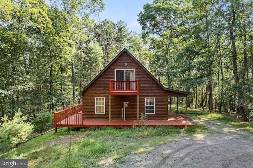 Adorable log cabin situated on over 5 acres for peace, quiet, and relaxation! Perfect for full time living or for a place to escape the hustle and bustle. The HOA states the property may not be used for an AirBnB. The front porch extends across the front and wraps around to the back of the home. You are greeted with an eye catching stone gas fireplace that extends to the high, vaulted ceiling. The kitchen and living room have hardwood floors and sliders that open to the deck. The open concept is perfect for entertaining and on the cool nights being able to open the sliding glass doors allows even more living space! There are 2 bedrooms, full bathroom with tub/shower, and stackable washer/dryer  on the main level. Upstairs is the primary suite with sliding door that leads to a private balcony to enjoy that perfect cup of coffee, and a half bathroom. There is an extensive whole house water filtration system located in the crawlspace. The septic was pumped in 2023. The HOA is $100/yr. Internet is provided by Hardy Net. Explore the 5.26 acres the property offers, and still head over to Lost River State Park that is only 4 miles away for more fun and adventure! The property is currently an AirBnB due to being grandfathered into the HOA, as a result showing days/times may vary and are limited at this beautiful time of year.
