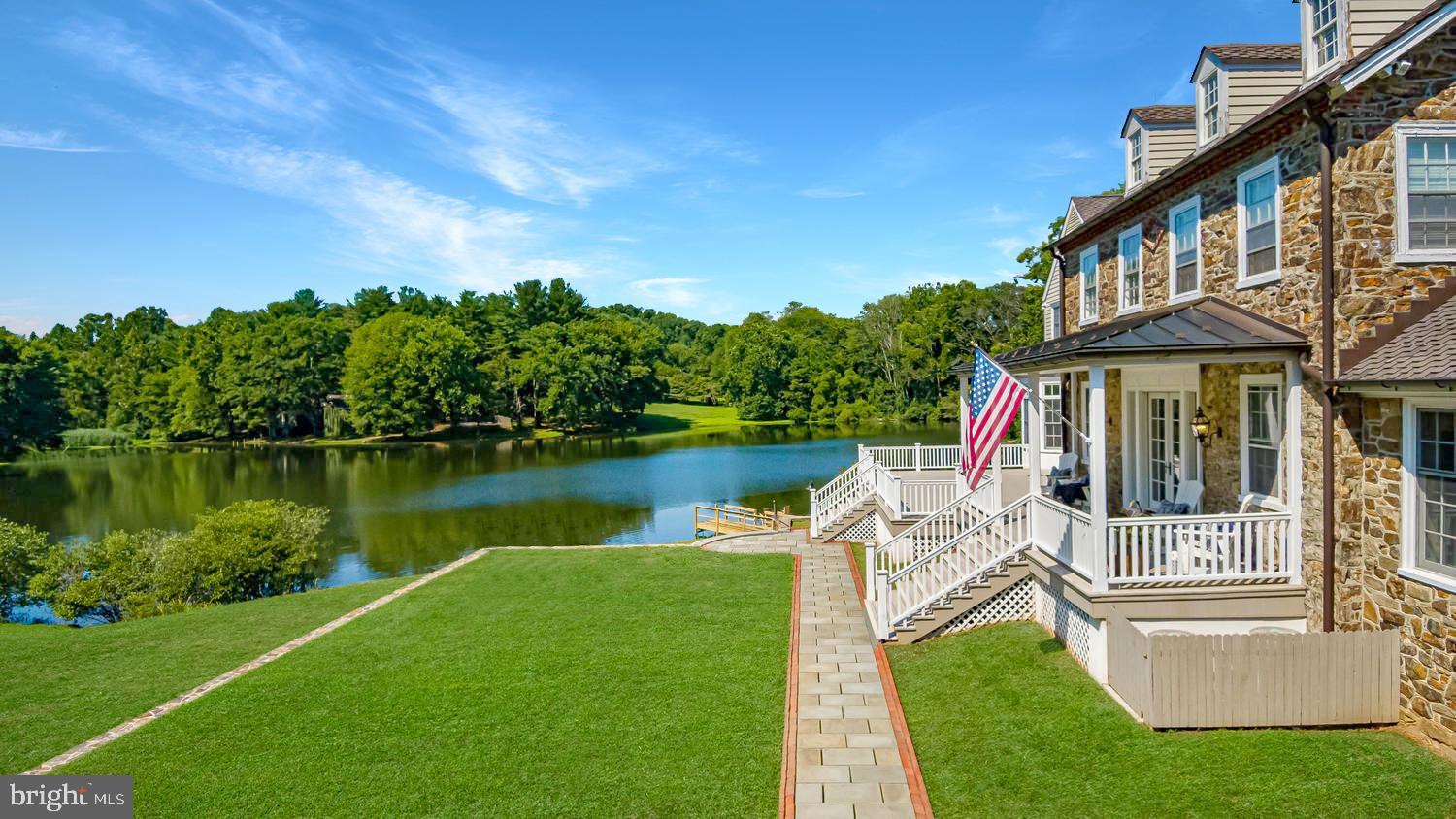 In the epicenter of historic Chadds Ford, Dewson Construction with top of the line craftsmanship and details, a classic Pennsylvania stone masterpiece is perched on the banks of Karver Lake. Embracing its 7-acre water front setting, the architectural heritage of an historic home is echoed in character with an expansive Archer-Buchanan designed home. With respect to its Georgian architectural vernacular but ushering in a lightened style and spacious aesthetic, all-important views are oriented toward the lake. The stone of an original jewel was carefully matched for use on the front facades and in the hardscape walls that frame the lawns. Natural light floods the foyer and grand staircase. Richly stained reclaimed white oak floors blanket main and upper levels, and provide classic contrast to the warm, neutral pallet. Paneled doors paired with meticulously reproduced and repurposed historical hardware punctuate every space with weight and scale amplified by 10' ceilings. Working from home takes on a delightfully new meaning in the pair of offices off the main entrance, or study on 2nd level. Maintaining the homes historical integrity, the gathering space opposite the offices features two original fireplaces, coffered ceilings and casually elegant dining. Beyond, an original stone wall and three window walls provide a sunny retreat for relaxation, home school or play. The dramatic heart of the home is carefully appointed with richly grained custom cabinetry and built-in fine appliances, topped with subtle stone and wood counters. French doors invite outside living with water front ringside seats to the changing seasons. The family friendly space with both banquette and bar stool seating spills into the comfortable family room with plenty of space for family and friends to sprawl. Stone fireplace, carved mantle and built-in cabinets that compliment those in the kitchen create architectural interest and charm. Main floor mudroom with built-in cubbies, laundry with copper potting sink, walk in pantry, walk in storage closet and two well appointed powder rooms fulfill every wish list and serve every need. Up the back stairs, the master suite offers the amenities and understated elegance of a four star hotel. Private walk in closets, bathroom accommodations for two take the amenities to a higher level, and tucked into the hallways a shoe closet, linen closet, suitcase closet and additional storage are skillfully arranged. Family and guests are well served in three additional spacious bedrooms, en suite. In a wing of the second floor, the second laundry, and au pair suite offer private accommodations and sitting room. Blending modern convenience and old world charm, the third floor plays host to two additional bedrooms, and bath, as well as bonus finished spaces. The daylight lower level has a fully appointed fitness suite, highlighted by a steam shower and separate sauna. A kitchenette adds service to the lounge area, craft space & play room. An accessory three bay carriage house enhances the integral two-car garage with ample additional storage for garden equipment. Bespoke details celebrate the medley of craftsmen enlisted for the lake house. And while quality is evident at every turn, the comfort and convenience of state of the art mechanicals add to the litany of attributes this property has to offer.