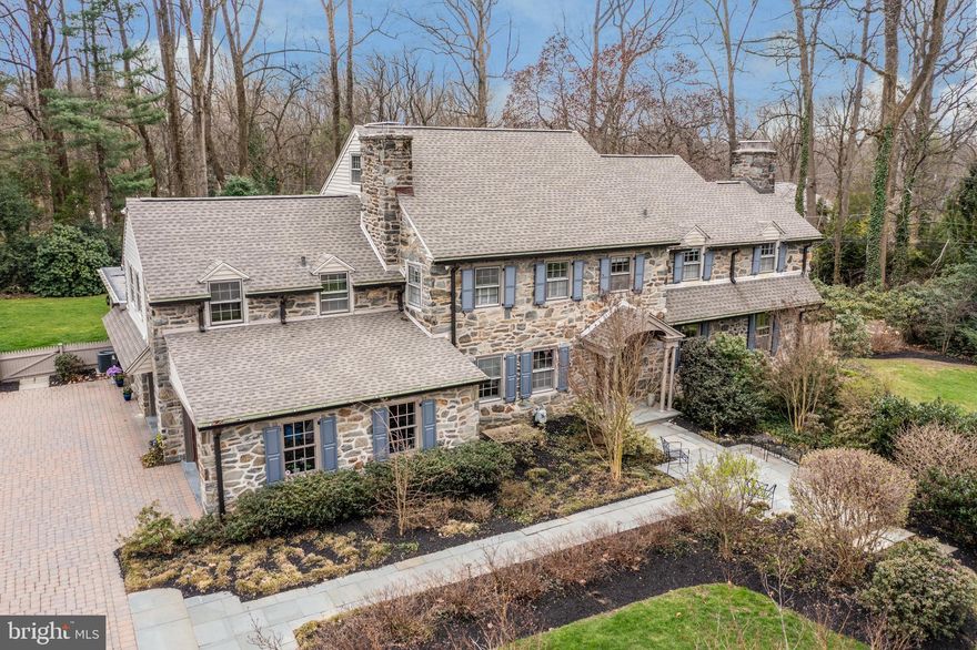 Stately yet comfortable, this lovely 5000 sq. ft. 5 BR, 6 BA stone colonial in Penn Valley combines stunning millwork and architectural gems from the original Chauncey estate mansion with a vast array of today’s most sought-after features. Among its many offerings are gorgeous hardwood floors, a main suite with a massive main bath, a large island kitchen, amazing family and office spaces, and a generous, flat lot, all ideally situated on one of Penn Valley’s most cherished streets. From the spacious entry foyer, step through the milled archway down to the living room with hardwood floors, a wood-burning, mantle-accented fireplace, deep-silled windows, and french doors to the bluestone patio that spans most of the rear of the home. To the left of the center hall entry foyer, another milled archway invites you to the dining room, offering 2 built-in lighted cabinets and its own wood-burning fireplace. Enter the kitchen with a quartz-countered center island that seats 5 and is studded with 4 pendant lights. Completely surrounding the island you’ll find abundant wood cabinetry, some with glass fronts, granite countertops, stainless steel appliances, and everything you’d expect in a high-end kitchen: gas cooktop with grill, built-in main oven, convection/microwave oven, warming tray, SubZero refrigerator, Bosch dishwasher, separate wine refrigerator and filtered water system. Continue from the kitchen to the exceptional family room offering a gas fireplace, floor-to-ceiling casement windows, multiple french doors that exit to the patio and yard, an exposed stone wall, skylights, and a full bath. This area also provides driveway access, closet space, and a separate access to the 2-car attached garage with epoxy flooring. Working from home will be no problem in the fabulous office teeming with natural light and built-in shelving. A hallway off the kitchen leads to the large, flat, fully-fenced and garden-ready backyard and patio. Up the center stairs is the main bedroom with 2 walk-in closets and more built-in storage, adjoined by a huge main bath complete with a tiled shower, private toilet room, jetted tub and double vanities topped with travertine tile. The upstairs level offers 2 additional, spacious en suite bedrooms with generous closets. A back staircase from the kitchen brings you to the 4th bedroom and hall bath, a cedar closet, and a 5th bedroom currently used as a combined 2nd office/laundry room. The lower level provides a great finished flex space that includes a game area, dance/exercise section, an arts-and-crafts corner, a decorative fireplace, and another full bath, plus a mechanical/storage room and an outside entrance. Bonuses include a 240 volt charging station in the garage, a paver driveway, and a walk-up attic that could be finished for even more living space! All the tremendous offerings of this lovely, expansive, stone colonial coupled with the convenience of its prime Lower Merion location and schools will make you thrilled to call it your new home.