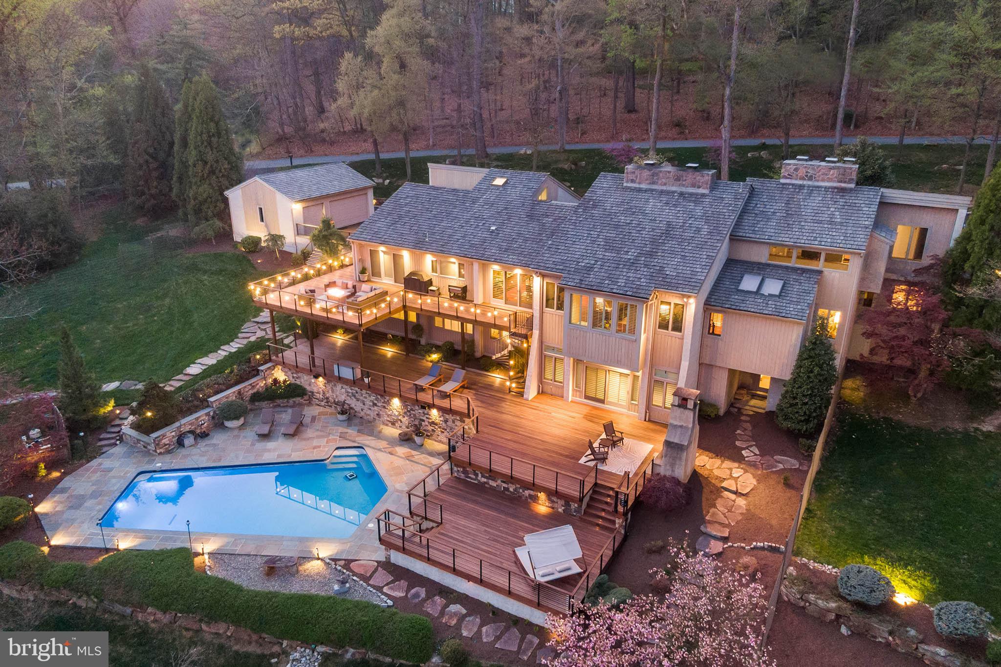 Modern & timeless luxury design with no detail overlooked! California dreaming? Not anymore! 1965 Rochambeau Drive is a truly spectacular home that sits on a quiet Cul-de-sac street in the award-winning and highly sought-after Tredyffrin-Easttown School District.
This exceptional contemporary home offers 5 beds, 5.5 baths and features 7,300+ sq. ft of interior living with smart home technology, African Mahogany hardwood floors, 4 fireplaces, a circular driveway and 6-car garage space. With nearly 3 acres of outdoor & indoor living space, the professionally landscaped property includes a chopping hut, teahouse, boardwalk, walking path and discreet deer fencing. The impressive 3,000 sq. ft IPE decks extend over 3 levels, overlooking the fully renovated in-ground pool. An elevator, full house generator, irrigation system, automated landscape lighting, and security system with cameras are only a few of the many features that accompany this home.
The PA blue flagstone front walkway leads guests through a new fiberglass custom double door with glass surround, where once inside, they are greeted by a spacious vaulted ceiling foyer and feature stone wall. From here, the home flows perfectly for everyday living and entertaining. A sunken den with fireplace offers a relaxing space to curl up with a book. The first-floor primary bedroom suite with sitting area is a true retreat, equipped with a gas fireplace, dressing area with washer/dryer unit, a primary bath with double vanity, separate tub & shower, towel warmer, radiant heat flooring and new sauna. The light-filled great room with its stunning fireplace and adjoining wet bar complete with beverage fridge, icemaker, dishwasher, and more, is truly conducive to hosting parties of all sizes! A formal dining area with French doors overlook beautiful Chester County’s lush greenery. The open and spacious kitchen is a chef’s dream, featuring top-of-the-line appliances including double Wolf ovens, Wolf 6-burner gas range with searer, Wolf plate warmer, separate full-sized Subzero refrigerator and freezer, two Bosch dishwashers, icemaker, built-in coffeemaker & microwave, reverse-osmosis water system, an oversized island, and a large breakfast room area with walk-out access to the oversized deck (perfect for grilling!).
Two separate upper levels offer privacy and maximize the full footprint of this expansive home. The bright main stairway by the foyer leads up to a landing and additional flex space for relaxing. An enclosed area could easily be converted into a 6th bedroom, with its full bath and balcony (currently used as an office suite). The other stairway by the kitchen offers an au-Pere suite above the 3-car attached garage, with full bath and plenty of closet space and its own HVAC zone. Both garages are fully finished with epoxy flooring, insulated drywall and 3 garage bays each. The beautiful attention to detail is sure to please the car lover looking to store “special” vehicles. The center stairway leads to the fully finished lower level, filled with natural light through the plantation shutters. The oversized family room with another fireplace and built-in surround sound, is an incredible space for watching the big game or enjoying family movie nights. The slider opens to the deck with an outdoor fireplace and patio walkways. Completing the lower level is a game room area with pool table, bar counter with icemaker, built-in bookshelves, 3 more bedrooms, 2 full baths, laundry room, temperature-controlled wine cellar, exercise/flex space room, smart home central station and a bonus flex space room with direct outdoor access.
No matter where you turn on this property, you’ll be blown away by the style and sophistication, unbeatable views and deluxe amenities. Simply unpack and start enjoying resort-style living!