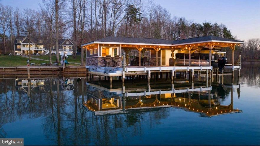 Extraordinary fully-furnished waterfront estate, perfectly set on the tranquil private side of Lake Anna, offering an unmatched blend of luxury, custom craftsmanship, and breathtaking natural beauty, along with high-speed fiber internet.  With 140+ feet of pristine shoreline and sweeping, unobstructed water views, this waterfront property presents a rare opportunity to experience a refined lake life.  Encompassing more than 5,600 square feet of thoughtfully designed living space, this home features seven generously proportioned bedrooms, including five private en-suite retreats, ensuring exceptional comfort and privacy.  Craftsman-inspired architecture is showcased throughout, highlighted by rich hardwood flooring, extensive custom trim work, chair rail, and other refined finishes.  The great room features soaring vaulted ceilings, custom built-in bookcases and shelving that frame an elegant fireplace crowned with a beautiful white mantle and stone work.  The large four-seasons room is encased by massive windows showcasing incredible views of the lake.  The expansive gourmet kitchen is designed for both entertaining and everyday living, featuring premium stainless steel appliances, a massive island graced by pendant lighting, a double wall oven, large gas cooktop, a built-in ice maker, beverage refrigerator, and an impressive walk-in pantry adorned with elaborate custom shelving.  The second floor offers two spacious primary suites, each with clear lake views, en suite bathrooms, and large walk-in closets.  The finished lower level further elevates the home’s entertaining capabilities with three additional bedrooms (one with a true functioning Murphy bed!), and a full-scale wet bar / kitchen with stainless appliances and custom stone work, creating an ideal space for gatherings and recreation.  Outdoors, the estate transforms into a private lakeside sanctuary set on a perfect flat lot showcasing incredible water views.  The custom-designed boathouse is a showpiece in itself, complete with a luxurious kitchenette, a vibrant tiki bar with roll-up windows, elegant granite countertops, a dedicated storage room, and a boat slip equipped with an electric lift. A sandy beach, a massive inviting hot tub, and expansive stone fire pit area with an abundance of outdoor furniture create the perfect setting for relaxation and unforgettable evenings along the water.  Adding both versatility and distinction, the property includes a completely finished attached garage with recessed lighting, built-in workspaces, cabinetry, and an extensive private primary suite above, offering exceptional space for guests, extended family, or creative use.  Surrounding the residence, meticulously curated landscaping and hardscaping wrap the property with breathtaking beauty, complementing the serene waterfront backdrop.  A 17-zone irrigation system keeps the landscaping fresh and hydrated.   Great location: close to groceries, restaurants, fast food, ABC, and more. This remarkable Lake Anna escape offers a rare convergence of elegance, privacy, and resort-style living, where every detail has been thoughtfully designed to deliver a truly exceptional waterfront lifestyle.  INVESTORS: short term rentals are permitted in this subdivision.  Lake Anna has been rated one of the top short term rental locations in the entire nation, and is home to some of the top-performing short term rentals in the Commonwealth of Virginia.  Purchase includes furniture, furnishings, decorations, appliances, and a significantly elevated lifestyle.