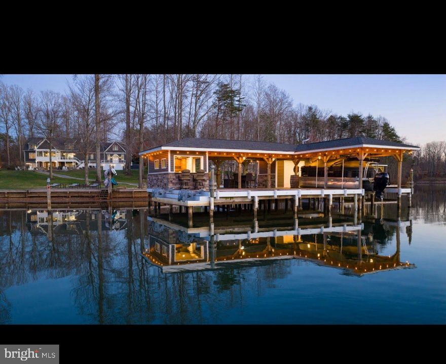 Extraordinary fully-furnished waterfront estate, perfectly set on the tranquil private side of Lake Anna, offering an unmatched blend of luxury, custom craftsmanship, and breathtaking natural beauty, along with high-speed fiber internet.  With 140+ feet of pristine shoreline and sweeping, unobstructed water views, this waterfront property presents a rare opportunity to experience a refined lake life.  Encompassing more than 5,600 square feet of thoughtfully designed living space, this home features seven generously proportioned bedrooms, including five private en-suite retreats, ensuring exceptional comfort and privacy.  Craftsman-inspired architecture is showcased throughout, highlighted by rich hardwood flooring, extensive custom trim work, chair rail, and other refined finishes.  The great room features soaring vaulted ceilings, custom built-in bookcases and shelving that frame an elegant fireplace crowned with a beautiful white mantle and stone work.  The large four-seasons room is encased by massive windows showcasing incredible views of the lake.  The expansive gourmet kitchen is designed for both entertaining and everyday living, featuring premium stainless steel appliances, a massive island graced by pendant lighting, a double wall oven, large gas cooktop, a built-in ice maker, beverage refrigerator, and an impressive walk-in pantry adorned with elaborate custom shelving.  The second floor offers two spacious primary suites, each with clear lake views, en suite bathrooms, and large walk-in closets.  The finished lower level further elevates the home’s entertaining capabilities with three additional bedrooms (one with a true functioning Murphy bed!), and a full-scale wet bar / kitchen with stainless appliances and custom stone work, creating an ideal space for gatherings and recreation.  Outdoors, the estate transforms into a private lakeside sanctuary set on a perfect flat lot showcasing incredible water views.  The custom-designed boathouse is a showpiece in itself, complete with a luxurious kitchenette, a vibrant tiki bar with roll-up windows, elegant granite countertops, a dedicated storage room, and a boat slip equipped with an electric lift. A sandy beach, a massive inviting hot tub, and expansive stone fire pit area with an abundance of outdoor furniture create the perfect setting for relaxation and unforgettable evenings along the water.  Adding both versatility and distinction, the property includes a completely finished attached garage with recessed lighting, built-in workspaces, cabinetry, and an extensive private primary suite above, offering exceptional space for guests, extended family, or creative use.  Surrounding the residence, meticulously curated landscaping and hardscaping wrap the property with breathtaking beauty, complementing the serene waterfront backdrop.  A 17-zone irrigation system keeps the landscaping fresh and hydrated.   Great location: close to groceries, restaurants, fast food, ABC, and more. This remarkable Lake Anna escape offers a rare convergence of elegance, privacy, and resort-style living, where every detail has been thoughtfully designed to deliver a truly exceptional waterfront lifestyle.  INVESTORS: short term rentals are permitted in this subdivision.  Lake Anna has been rated one of the top short term rental locations in the entire nation, and is home to some of the top-performing short term rentals in the Commonwealth of Virginia.  Purchase includes furniture, furnishings, decorations, appliances, and a significantly elevated lifestyle.