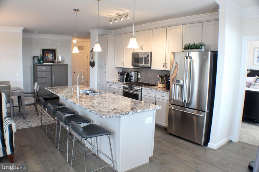 Like NEW (2018), stunning 1330 sq. ft.  5th floor (Top Floor!) corner unit, light, bright and quiet condo. Full of upgrades! Features foyer, open concept living, dining and kitchen with beautiful low maintenance wide-plank hardwood floors, lots of windows and gas fireplace. Kitchen has GE Café stainless appliances, large center island with seating, and gas 6-burner stove. Kitchen also features granite countertops and tile backsplash. Laundry area with LG full size w/d. Primary bedroom ensuite has walk-in closet, 2nd closet and bathroom with shower, 2 sinks and ample cabinet storage. Second bedroom includes double, custom organized closets and ensuite bathroom with tub shower and sink perfect for guests. Second bedroom also features custom Murphy bed with 2 separate office desks, book cases and file storage drawers.  Bed folds away when guests leave and the work day begins! Murphy bed can also be removed - totally optional!! Upgraded lighting throughout! Southeast facing balcony perfect for morning coffee or afternoon relaxing. Condo building has an elevator and includes deeded, covered one-car garage space. Convenient location with easy access to Dulles airport, restaurants and shopping. Steps to new Senior Center. Close to Chick-fil-a, Wawa and more! Flexible Close!