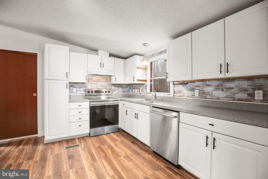 The smell of fresh coffee drifts through an airy kitchen as sunlight spills across refurbished wood shelving and a brick backsplash, bouncing softly off sleek stainless appliances. A quiet morning unfolds just beyond the windows—five private acres stretching out beneath mature trees, tucked near the end of a non-thru street. Peaceful, but never isolated.

Inside, 1,250 square feet of thoughtful updates capture attention immediately: exposed beams draw the eye toward vaulted ceilings, a stylish feature wall anchors the family room, and wide-plank wood laminate flooring flows throughout with warm, cohesive character. Every detail feels intentional, right down to the Smart House upgrades—voice-controlled smart plugs throughout the interior and Blink Security floodlights positioned at the front and rear, bringing both convenience and peace of mind.

The kitchen wasn’t just updated—it was reimagined. Clean lines in white cabinetry, a modern layout with updated countertops, and handcrafted open shelving offer personality as well as function. Both bathrooms heighten the design aesthetic, with fresh tile, contemporary vanities, and a new walk-in shower in the ensuite.

Comfort extends to the essentials: a new well pump (2023), an expanded front deck (2021), and a newer roof (2017). Step outside and the lifestyle unfolds even further. A pair of versatile sheds hold tools, equipment, or hobbies. A chicken coop offers a chance to collect your own morning eggs. The carport keeps vehicles protected, while the broad, usable acreage boasts cherry, peach, and pear trees and invites gardens, orchard plans, weekend bonfires, and small-scale homesteading. With no HOA, the land here belongs fully to those who call it home.

A retreat that allows life to slow down when needed, yet sits surprisingly close to shopping, restaurants, and major highway access. Updated, turnkey, and ready for the lifestyle you choose to build upon it.