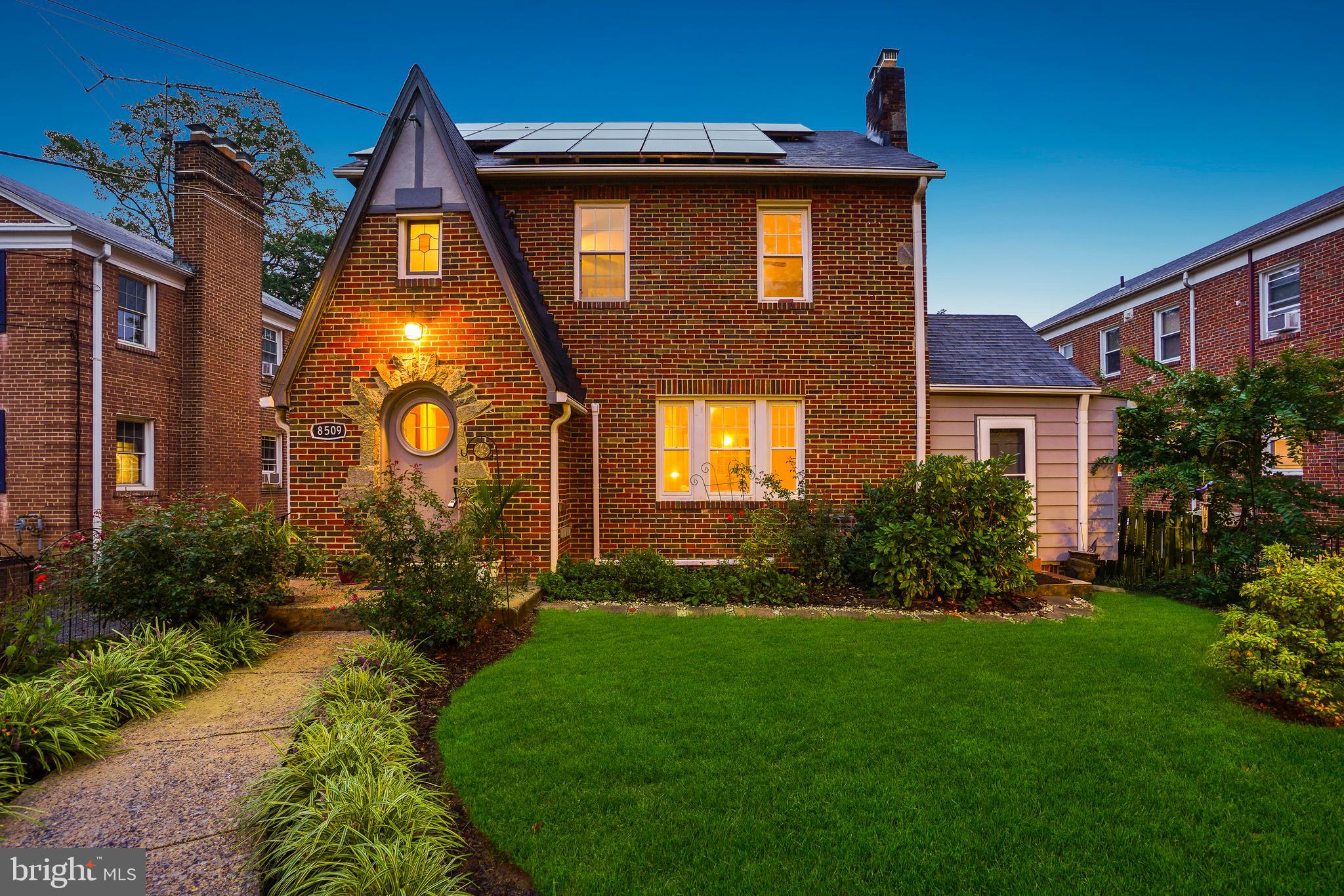 PURELY MAGICAL! This brick-and-stone Tudor blends timeless character with thoughtfully designed spaces that combine historic charm and everyday comfort. Built in 1937, this distinctive residence includes a bevy of bedrooms, four full bathrooms, and a detached two-car garage with a large, lofted bonus space.
Upon entry, you’re welcomed by a classic arched front door with a portal window, leading into engaging living areas. Four levels of striking architectural details include hardwood floors, vaulted ceilings, and refined lighting. The spacious living room features a stone fireplace and a built-in bar, while the dining room flows seamlessly for entertaining. The newly renovated kitchen impresses with solid-surface counters, custom cabinetry, a gas range, and stainless-steel appliances. The main level is complete with a bedroom/sunroom with vaulted ceilings and a fireplace, a full bathroom, and a cedar hall closet.
The second floor offers three freshly painted bedrooms and two updated bathrooms, including a primary suite with a stylishly renovated bath. The third level provides versatile space for a playroom, guest area, or office. The lower level includes a bright recreation room, a full kitchen, a private bedroom/in-law suite, a full bathroom, laundry, and storage.
The home is enhanced with owner-owned solar panels and a newly installed (June 2025) mini-split air conditioning system.
Outdoors, the property features mature trees and lush landscaping with flowering plants and multiple crepe myrtles. Perennial gardens bloom year-round. The rear yard offers privacy and a secure space for relaxation and play, complete with a patio and brick fireplace. The fully insulated detached two-car garage includes a lofted bonus space above, with potential for conversion to additional living quarters or rental use.
This truly remarkable property offers wonderful urban living just moments from all the vibrant amenities of Takoma Park. This home’s location combines the best of urban accessibility with access to nature. Situated just steps to historic Old Takoma business district, blocks to the Sligo Creek’s bike and walking trails, parks, and playgrounds, Koma café, forthcoming Purple Line, and readily accessible to the Red Line metro. The home is in close proximity to downtown Takoma Park and downtown Silver Spring and all the amenities these locations offer, including restaurants, coffee shops, farmers markets, gyms, and live music venues.