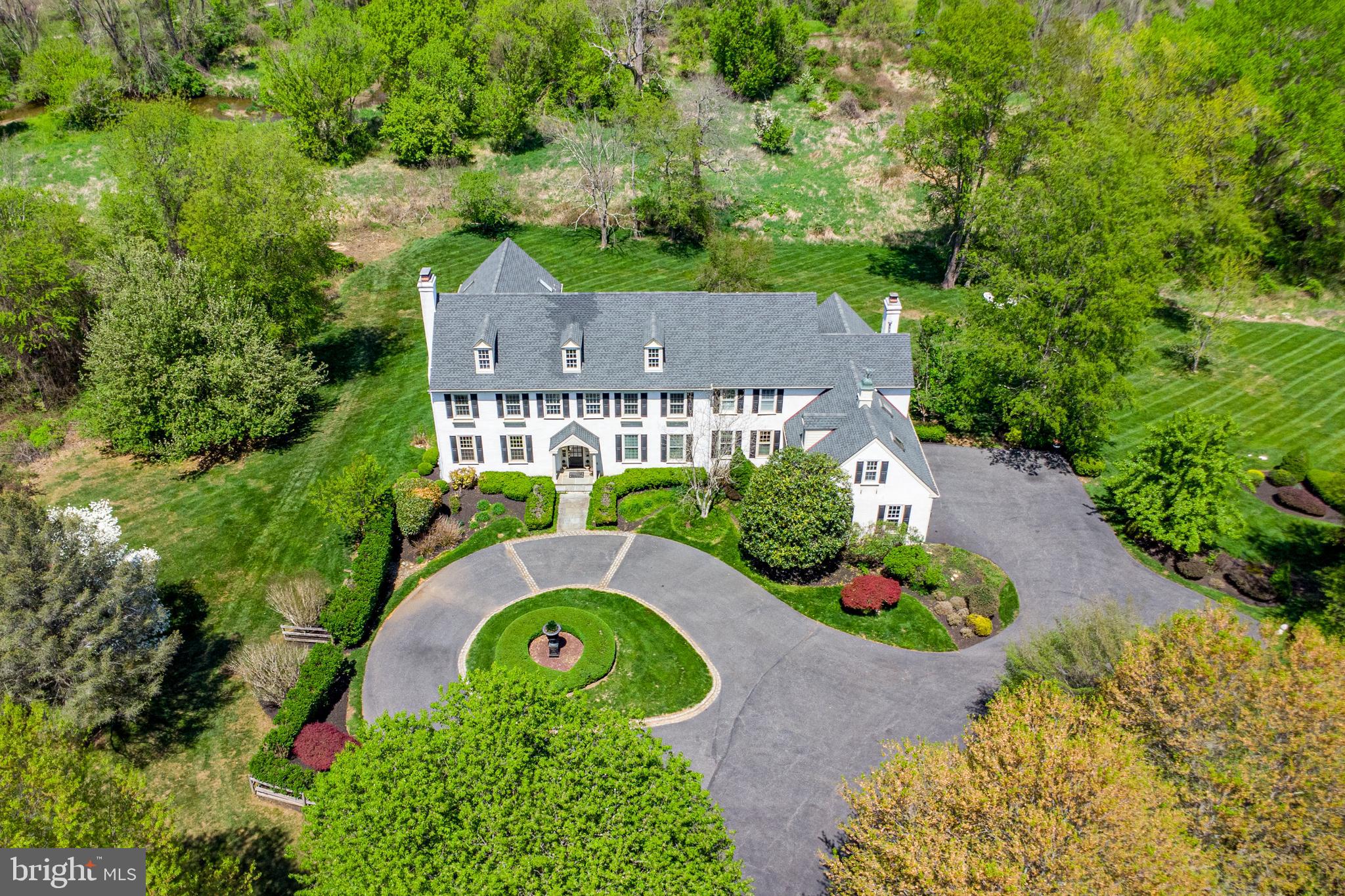 Welcome to Wildbanks, a home offering 6,075 sq. ft. of refined livability in a one-of-a-kind, private setting. Sited down a long drive off a quiet cul-de-sac in the sought-after Bainbridge neighborhood, this exceptional home blends community at the front with seclusion at the rear. The property backs to protected township parkland, ensuring that its idyllic views remain forever preserved. Named for the two streams that meet on its grounds, this 11.9-acre estate is largely left in its natural state. It’s a haven for local wildlife—deer, foxes, rabbits, turtles, and countless birds—who share the land’s open lawns, wooded areas, and meandering waterway. Though the setting is serene, the location is also highly convenient—just 15 minutes from the charming college town of West Chester, with its vibrant downtown, university community, dining, and cultural offerings. Inside, every detail reflects a balance of beauty and functionality. Wildbanks has been meticulously designed to accommodate elegant entertaining and busy family life. Meant to evolve with the changing rhythms of a family, the home delivers both comfort and sophistication, with six bedrooms, five and a half bathrooms, multiple gathering spaces, and abundant storage. Upon entry, a double-height wainscoted foyer, crowned by a vintage chandelier, sets the tone with unexpected flair. A graceful staircase and glass doors overlook the tri-level rear deck. Flanking the foyer, the formal living and dining rooms feature exquisitely detailed hardwood floors. The living room, with a wood-burning fireplace, leads to a sunken vestibule and an elegant powder room—complete with a marble standing shower cleverly concealed to also serve an adjacent bedroom. Across from the dining room, a butler’s pantry offers a wet bar with a secondary dishwasher and the pass-through to the kitchen streamlines both entertaining and cleanup. The chef’s kitchen is a dream, equipped with two sinks, high-end appliances (including a 48” refrigerator, double ovens, gas cooktop, warming drawers), and a walk-in pantry. French doors lead to the spacious family room, where massive windows and a grand wood-burning fireplace creates a welcoming connection between the indoors and nature. A mudroom, charming laundry, additional powder room and oversized coat closet with built-in storage complete the main floor. The walk-out lower level offers a flexible layout that can serve as a private in-law or au pair suite. It includes a fully mirrored and well-equipped gym, a lounge with wet bar, electric fireplace and TV, a wine room with variable temperature wine storage, and a generously sized guest bedroom with a walk-in closet and full bath that also serves the living area—ideal for long-term guests, multigenerational living, or live-in help. Upstairs, a couple’s dream office/library awaits with a gas fireplace, two built-in desks, library stacks, and a sunlit window seat beckoning young readers. Three additional bedrooms—each with walk-in closets—share a hall bath and a Jack-and-Jill bathroom, all thoughtfully designed with linen closets and family-friendly tub/showers. Robern medicine cabinets add convenience. Alone, at the end of the hall, is the owner’s retreat. Double doors open to a capacious sun-filled bedroom with a gas fireplace visible from the bed. A second set of doors leads through dual dressing rooms to the spa-like primary bath, where a freestanding tub rests on a marble “carpet” amid radiant heated floors. A dual-person stall shower offers a refreshing complement to the soaking tub, while an electric fireplace and built-in TV make necessary daily rituals feel special. Custom cabinetry accommodates every need, with features like a makeup vanity, salon drawers, a towel warmer, and a hidden refrigerator. This exceptional home must be experienced to be truly appreciated. It offers a rare harmony of luxury, livability, natural beauty, and accessibility.
