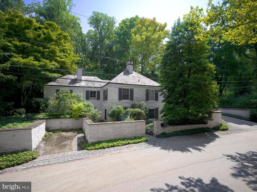 Welcome to this charming residence on Avon Road in Haverford, originally the gatehouse to the grand "Avonwood" estate. This historic property retains original entrance pillars and stone walls and is set amidst beautiful, serene surroundings on a quiet road with little through traffic. The painted stone home features a slate roof, flagstone walkways, and Belgian block details.  Enter through the lattice arch and follow a trellis-covered flagstone walkway along a peaceful courtyard to the main entrance. The foyer, which boasts terra-cotta tiled flooring, offers a warm welcome and includes a staircase leading to the lower level. The bright, spacious living room has large windows with two exposures plus two sets of French doors that open to the courtyard.  It also includes built-in display cabinetry, a large wood-burning fireplace, and captivating views of the grounds. An elegant dining room is accessible through two sets of tall doors from the living room and a swinging door from the kitchen. This large room features moldings, hardwood flooring, and built-in lighted display and storage cabinetry. The walls were hand-painted by PAFA artist Iwan Nazarewicz. Windows on two sides, including a wall of sliding glass doors, open to the rear flagstone terrace. A nearby den, with its cozy gas log fireplace, built-in bookcase and moldings, connects to both the living room and eat-in kitchen, and makes an ideal retreat for reading and relaxation. The kitchen, blending functionality with charm, features a cushioned window seat for casual dining, tall wood cabinetry, a triple stainless sink, bar sink, and appliances including a KitchenAid 4-burner gas cooktop with grill and double wall ovens. The primary bedroom, located on the first floor, has exquisite Zuber wallpaper and a hidden king-sized Murphy bed behind wall panels. French doors open to the courtyard and bring in natural light. The primary bath includes a vanity with double sinks and a shower with multiple side sprays.  An adjacent small bedroom, which can also be used as a dressing room, has windows on two sides and three closets. A nearby powder room adds convenience and style. The lower level is daylit with walk-out access to the front walled garden’s roses and camellias.  There is a bedroom suite with windows on two sides, a closet, and a full bathroom with a tub/shower, which is perfect for guests or as a separate living space. This level also includes a sitting room, a large storage closet, and a room that could serve as another bedroom or fitness area.  It has bookcases and double doors to the front garden.  A small utility/office area ends at a laundry room.  The expansive rear grounds include a large flagstone terrace with stone knee walls, an ivy-covered wall, multiple flower gardens, and a wide stone staircase ascending to a meadow. From there a path leads through the woods to a back gate on Avonwood Road. A separate structure, inspired by the architecture of European orangeries, houses a stunning 50-foot indoor lap pool with a glass roof.  Mature trees provide privacy, while a detached two-car garage has convenient French doors opening toward the home and courtyard. This property combines historic charm and modern expansions, set in a peaceful, private woodland. The fully fenced grounds include multiple gardens and sitting areas. The flexible floor plan of the home adapts to many lifestyles.  This historic oasis on the Main Line is a private sanctuary for luxurious living, all within convenient walking distance to the Haverford and Bryn Mawr train stations.