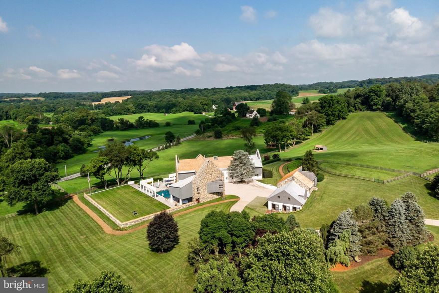 This phenomenal 8,500+ sqft home may be the most fascinating, intriguing home on the market today! Set on 14.6 acres across three parcels, and mixing both traditional and contemporary features, this home looks like a wonderful Chester County stone barn conversion at first glance. Sensitive to the property's historic setting which overlooks the Brandywine Valley and the very roads General Howe used to flank General Washington at the Battle of the Brandywine, the owner sought to incorporate native fieldstone walls and cedar roofs. These traditional textures enhance the design's bank barn feel, accented with eye-catching architectural details. One enters the home into a bright Foyer which features a ceiling shaft soaring more than 35 feet to the top skylight. Straight ahead are large glass panels that offer stunning views of the property's pastures and plantings. To the right is the Living Room with a plush carpet on which the Brandywine Creek's course is illustrated. Down an interesting hallway is the home's peaceful Office complete with a fireplace and rich cherry raised paneling and custom shelving. The Dining Room boasts a curved wall of glass panels and wood flooring that came from the landmark 1906 Sears Building in Chicago. The Family Room offers a soaring ceiling, fireplace, a large bar with pass through to the Kitchen, and lots of glass with stunning views. Off the Family Room is a large patio with a pool and the ever-present fabulous views of the surrounding countryside. The gourmet eat-in Kitchen features high-end stainless appliances, ample Italian and custom cabinetry, along with plenty of workspace. A large three-car, heated Garage is easily accessed from the Mud Room. Upstairs are two bedrooms joined with a Jack-and-Jill bath, Laundry, Guest Room with en-suite bath, and a gracious Master Suite. The Master Suite offers numerous amenities: a wall of windows with automatically retracting blinds at the foot of the bed to unveil incredible views, a private porch, fireplace, walk-in closet, shoe closet, incredible bath, and an upper level which offers additional space for meditation, office, or hobbies. At the end of a hallway is a huge Gym with a stone wall, lofted ceilings, an oversized steam shower, and plenty of space for all of your exercise equipment. Wine enthusiasts will love the wonderful wine cellar in the sub-basement, twenty feet below ground level, affording the perfect temperature. The barn offers ten large box stalls, a tack room, and a garage area for all your equipment. The barn's upper level, with on-grade access, offers a massive loft with volumes of space plus a workshop area with a powder room. This home has been well cared for and loved. All of the roofing is new and the property has been impeccably maintained. This is a true showcase property!
