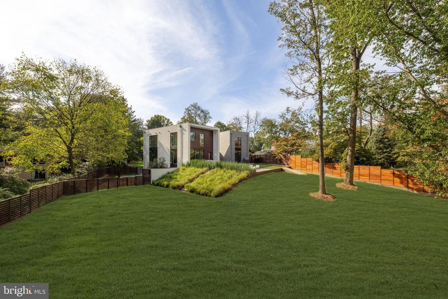 Nestled amidst the verdant bends and winding hills of Chevy Chase, 9119 Levelle Drive is a
textbook showcase of cutting edge modernism.  Designed in 2021 by the acclaimed Robert M.
Gurney, FAIA and built by the renowned Peterson and Collins Builders, the extraordinary skill and craftsmanship is evident throughout and unparalleled.  This singular home is yet another award-winning example of geometry, brilliant manipulation of light, artistic use of glass, and conformation with its natural surroundings. Prominently sited on a coveted lot of just under an acre, towards the end of a no-through road, the approaching driveway opens into a rectangular motor court. Two likewise rectangular volumes are situated in a narrow ‘V’ configuration, connected by a glass bridge housing the front door. A transverse
gallery introduces the fully open concept main level by its informal spaces first. The chef’s
kitchen anchors said space, blending design and function with floor-to-ceiling minimalist, light
wood cabinetry concealing a comprehensive suite of commercial-grade appliances. An
extraordinary oversized center island, clad in light stone slabs with integrated seating and
waterfall edges, spans the entire length of the room. A flooring change from wood to tile, both
outfitted with radiant heat, signifies the transition into the adjacent light-filled breakfast area. A
generously proportioned, continuous living and dining area comprises the majority of the main
level. The latter is backed by full-height panes of glass, letting in tranquil wooded views. The
former, anchored by an abstract half-wood half-mosaic fireplace wall, interacts with said views
via a wall of glass which can be opened to blur the relationship between indoor and outdoor
living. The central staircase, artfully crafted from wood and glass, is both a showstopper and a
structural feat, which connects all levels of the home. The upper level contains private quarters,
including a stunning primary suite resting amidst the treetops. It features generous closet space
with custom built-ins, and the ubiquitous spa-inspired bath with a soothing ambiance attributed
to neutral woods and large panes of glass, as well as all the usual accoutrements. Secondary
bedrooms are well-proportioned, luxuriously finished, and arranged so as to maximize privacy.
Across the glass bridge is the second volume, clad in dark ground face block to contrast the
main volume’s white stucco. On the ground level, it houses an oversized garage with a frosted
glass door as well as a cozy living space. Upstairs is a fully self-sufficient apartment. The
kitchen mirrors that of the main residence, with full-size SubZero and Viking appliances, and a
peninsula island overlooking wooded views beyond the adjacent living area. A private bedroom
featuring a large walk-in closet, as well as a luxurious fully-tiled bath complete the unit.
Enclosed by full fencing constructed of mahogany and steel, the rear lawn comprises terraced
outdoor living spaces designed to engage with the lot’s topography. They include dual-level
patios with a fire pit, ideal for al fresco entertaining, dining, or lounging on a crisp autumn
evening. Further beyond, private rolling hills are surrounded by total privacy. Convenient to the
shopping, dining, and entertainment of both downtown Bethesda and Chevy Chase, as well as
the Nature Conservatory and trails along Beach Drive and major commuter routes, the location
is enviable. Not to be replicated in its architectural significance, 9119 Levelle Drive is a true one-
of-a-kind offering.