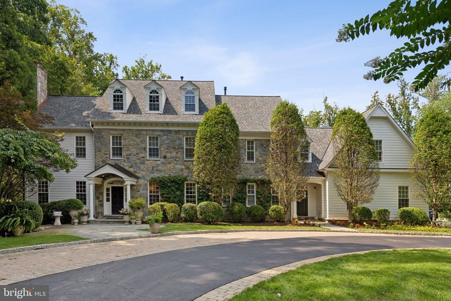 One of Potomac Village’s Finest Estates — A Classic Colonial Manor of Prestige and Timeless Elegance

An extraordinary offering in the heart of Potomac Village, this opulent 7-bedroom, 7 full bath, 2 half bath manor represents the pinnacle of architectural refinement and gracious living. Blending the enduring sophistication of classic Colonial design with bespoke modern luxuries, it stands as one of the most distinguished estates to come to market in recent years.

Approached by a sweeping circular drive, the home’s symmetrical stone façade, dormer windows, and stately pediment entry create a commanding sense of arrival. Inside, over 6,000 square feet of exquisitely appointed living space is designed for both grand-scale entertaining and intimate daily life. Sunlit formal rooms feature bespoke millwork, gleaming hardwood floors, and expansive windows framing the estate’s manicured grounds.

A gracious living room offers a refined setting for gatherings, while the formal dining room, crowned with a romantic glass chandelier, sets the stage for unforgettable evenings. The handsome library/home office is richly appointed with exquisite custom wood built-ins, creating a distinguished space for work or quiet retreat. The chef’s kitchen, equipped with professional-grade appliances and refined finishes, flows effortlessly into the expansive family room, each opening to the home’s outdoor living areas.

Upstairs, the primary suite is a private sanctuary with a spa-inspired bath and serene views, while additional en suite bedrooms provide comfort and seclusion for family and guests. The finished lower level offers purpose-designed spaces for recreation, fitness, and media, along with abundant storage.

Outdoors, the property unfolds into a parklike landscape reminiscent of a classic English garden—tiered lawns edged with boxwood hedges, meandering stone pathways, and seasonal bursts of hydrangeas, peonies, and climbing roses. Mature oaks and flowering dogwoods provide a natural canopy, while ornamental cherry trees, tulip magnolias, and curated perennial borders add a painterly quality to the grounds.

Multiple private garden rooms and sun-dappled terraces are thoughtfully positioned for morning coffee, afternoon gatherings, or twilight entertaining. At the heart of this pastoral setting lies a spectacular infinity-edge pool with a cascading waterfall, its reflective surface blending into the horizon and offering a tranquil focal point for the estate’s lush surroundings.

For the collector, the five-car garage offers exceptional space for prized automobiles, additional storage, or a workshop. This rare sanctuary, with its Washingtonian-worthy botanical artistry, is just moments from Potomac Village, Bethesda and minutes from top-tier schools, fine dining, and major commuter routes.

A true estate of distinction, this residence embodies prestige, architectural heritage, and an unrivaled standard of livability.