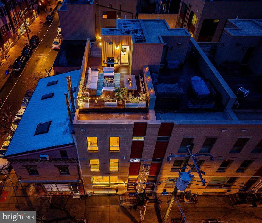 Located within Bedford Estates, a sought-after gated community towards the eastern side of Bella Vista where it borders Queen Village, stands a rare 20-foot-wide contemporary residence in the coveted Meredith School catchment. 622 S 7th Street offers 4,035 square feet of refined living space including 4 bedrooms, 4 full bathrooms, and 2 half baths, a finished lower level, private backyard, panoramic roof deck, gated parking with EV charger, and an elevator servicing every level of the home. Designed for luxurious everyday living, the home offers dramatic scale, abundant natural light, generous room proportions, and excellent storage throughout.

Facing east, oversized front windows welcome soft morning light, while the west-facing rear fills the home with warm afternoon glow — enhancing the dramatic ceiling heights and airy proportions throughout.

The first floor encourages entertaining and everyday comfort. The rear living room impresses with 12+ foot ceilings, a wall of windows, and direct access to the private patio and gated parking. A striking central light fixture anchors the space while a large walk-in storage closet adds practicality.

The gourmet kitchen is beautifully appointed with a stainless steel Wolf cooktop, double wall ovens, an extra-large Sub-Zero French door refrigerator, beverage fridge, and custom cabinetry with under-cabinet lighting and built-in storage solutions. The expansive eat-in island and countertops are finished in white marbled Quartz, creating a dramatic centerpiece for gathering and entertaining. The kitchen flows seamlessly into the dining area, highlighted by a designer chandelier and architectural ceiling detail.

Just off the main living area, the powder room makes a memorable design statement with stunning European wallpaper featuring rows of white bookshelves.

Beyond the kitchen, the elevator finished with hardwood flooring services every level of the home — including the finished lower level and the roof deck.

Modern smart-home features include WiFi-enabled Lutron lighting, Nest thermostats, motorized blinds, and built-in speakers wired for sound in the kitchen and on the roof deck.

Ascending the floating wood and metal staircase, the second floor offers a large storage closet and two spacious bedrooms, each with ensuite bathrooms and walk-in closets with custom storage systems. The rear suite features a tub/shower combination, while the front suite includes a sleek walk-in shower. Custom wallpaper adds warmth and personality.

The entire third floor is devoted to the primary retreat. Enter through a custom 4-foot-wide entry door into an expansive bedroom thoughtfully designed to accommodate a private en suite office. Dual walk-in closets provide generous storage.

The primary bathroom is spa-like in scale, featuring a freestanding soaking tub beneath a statement chandelier, dual vanities, and an oversized walk-in tile shower with built-in bench. A conveniently located powder room on this level services rooftop entertaining.

Above, the incredible roof deck offers sweeping city and river views, exterior lighting, built-in speakers, and ample space for lounging, dining, and grilling — a true outdoor living room in the sky.

The fully finished lower level continues the impressive scale with 12+ foot ceilings, a large media or recreation room, extensive storage, a mechanical room, and a private fourth bedroom with a full bathroom ideal for guests, gym use, or an in-law suite.

The Bedford Estates community offers secured gated entry, gated parking directly behind the home with a Tesla EV charger, and a resident dog park — rare amenities in this neighborhood.

Perfectly positioned in one of Philadelphia’s most vibrant neighborhoods, this home offers incredible access to community favorites like . Seger Park, Palumbo Park, Washington Square, Rally Coffee (just across the street), Emmy Squared, Mawn, the Italian Market, Whole Foods, and countless cafés, restaurants, and shops.