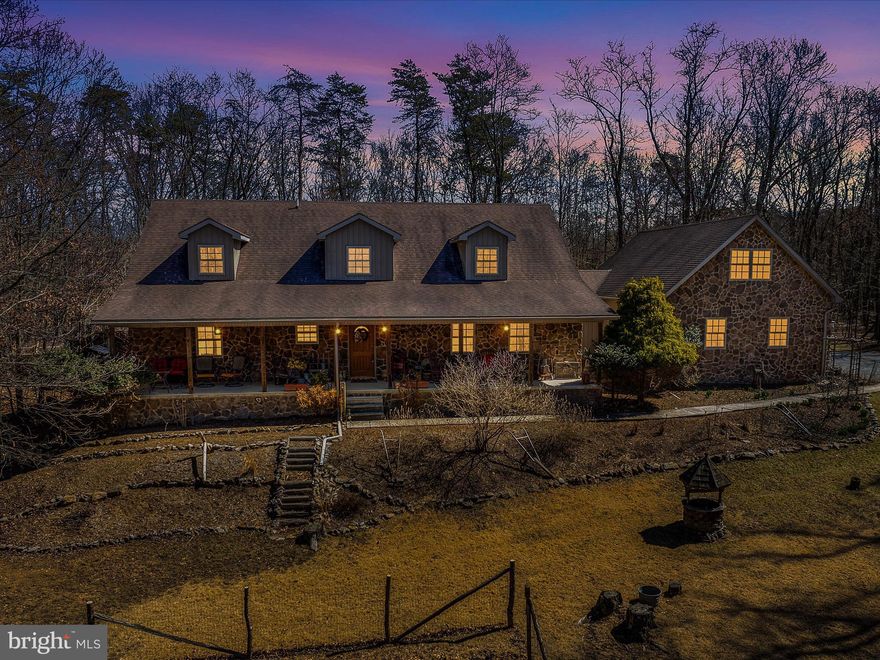 MOTIVATED SELLER!  This exquisite custom-built stone residence boasts an array of impressive features. Upon entering from the covered front porch, one is greeted by the expansive entry foyer. The living room showcases a stunning floor-to-ceiling stone wood-burning fireplace, high vaulted ceiling, and open staircase. A formal dining room and eat-in kitchen with quartz countertops, range, refrigerator, dishwasher, microwave, and ample cabinetry provide the perfect setting for large family gatherings. The main level primary bedroom suite offers two bathrooms, two walk-in closets, and a cozy sitting room. Additional features on the main level include a half bath and a sun porch overlooking the wooded backyard. A three-car garage provides access to the mud room/laundry hookup, and a finished room above the garage offers additional living space. The upper level features two spacious bedrooms, a full third bath, and a loft area with balcony overlooking the living room.  Full basement gives you lots of storage space.  A heat pump, central air, and outdoor wood furnace ensure a warm and cozy atmosphere throughout. Situated on 12+ acres comprising of 2 lots, this property is conveniently located on the north end of Berkeley Springs for easy access to I70.