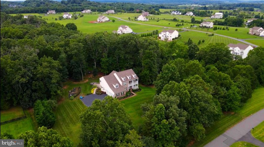 This exquisite Colonial-style home with its classic and stately presence is nestled on a beautifully landscaped, over 4 acres of wooded privacy offering a harmonious blend of luxury and comfort, perfect for those seeking a slightly rural lifestyle with a gentle touch of modern living in the exclusive and sought-after community of Huntleigh in Creighton Farms. This exceptional 5-bedroom, 4.5 bath custom estate offers over 6000 sq. ft of modern luxury living space with over $400K in premium upgrades.  This home features a symmetrical design with its front façade anchored by a covered porch with white columns that extend across part of the house, giving it a traditional and welcome look. Above, a second-story balcony that mirrors the porch below, adding both charm and architectural interest to this stunning home. The main level showcases a welcoming open grand entry with a rich and oak stained handrail and white spindles contrasting nicely against the darker wood steps. Straight ahead, a gorgeous gourmet kitchen featuring high end custom cabinetry, upgraded countertops, the heart of this home boasts a brand-new Wolf cooktop, double ovens, microwave, dishwasher, and oversized entertainment’s island along with a coffee/wine bar and lots of counter space making it ideal for your everyday living and entertainment on a grand scale. Flanked by a huge walk-in pantry and a mud room. Beautiful dark Engineered hardwood floors predominantly throughout, where you will find a warm and sun filled sunroom overlooking a private estate and mature trees. Entertain in the elegant dining room adorned with crown and chair rail molding, or gather in the formal living room for intimate moments The bright main-level office provides productive work-from home. Upper level, the primary suite has a beautiful chandelier, a stunning sitting room and a spa like bath with tub, shower complete with His/Her vanities, and an oversized walk-in closet. Two full baths with a shower and tub with Kohler fixtures. The finished lower level features a 5th bedroom with en suite with full bath, a game room, multiple areas for your own creation and two storage spaces. The walk-up basement provides a retreat featuring an extensive custom patio, fire pit and built-in grill, a 6 zones underground irrigation system and professional landscape lighting with a private alcove for relaxation and/or entertainment. The crown jewel at Creighton Farms is the 18-hole Jack Nicklaus championship golf course that you can join with additional membership. The expanded driveway leads to three car garage doors and 8 additional parking spaces. Situated on over a private 4-acre lot surrounded by nature, well-manicured walking trails, panoramic views of the gently rolling countryside, a serene creek, this one-of a-kind property feels tucked away yet remains conveniently close to the airport, railway, shopping, dining, and the Dulles Toll Road. Welcome Home!