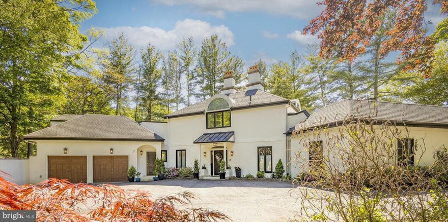 In the heart of Chestnut Hill, this exceptional European-inspired contemporary residence offers a rare blend of architectural living, organic warmth, and seamless connection to nature. Privately tucked behind a stately wall on nearly half an acre, the 5-bedroom, 5.1-bath home feels quietly removed from the everyday while remaining just moments from the Wissahickon, Germantown Avenue’s celebrated shops and restaurants, and convenient access to Center City. A gated driveway leads to a heated attached two-car garage with interior access, with infrastructure already in place for electric vehicle charging — reinforcing the home’s sense of privacy, comfort, and ease.
Beyond the bright, gallery-like entry, the eye is immediately drawn through the home toward its dramatic centerpiece: a spectacular glass conservatory rising at the rear of the residence like a private botanical pavilion. Flooded with natural light and framed by treetop views, the space blurs the line between indoors and out, anchored by a soaring antique chandelier and an oversized fountain repurposed as a sculptural planter. More than simply a sunroom, it is the architectural heart of the home — and the room you will inevitably find yourself gathering in.
Designed for both large-scale entertaining and intimate everyday living, the surrounding spaces balance modern luxury with warmth and texture. The living and dining rooms flow seamlessly into the conservatory, while a custom built-in wine and spirits cabinet reinforces the home’s effortless entertaining aesthetic.
At the center of the home, the warm contemporary kitchen combines clean lines, professional-grade appliances, skylit natural light, and understated functionality. Just beyond, a sunlit breakfast room or reading lounge with shelving opens onto a covered veranda overlooking the surrounding landscape and mature trees — an inviting setting for morning coffee, conversation, or quiet work-from-home moments.
A dramatic vaulted family room introduces a moodier counterpoint to the home’s airy entertaining spaces, pairing rich tones, oversized windows, a statement mantel, and integrated office alcove to create a comfortable lounge-like environment for relaxing or working from home. A nearby main-level laundry room adds everyday practicality.
Designed with comfort and privacy in mind, all five bedrooms feature ensuite baths. The main-level primary suite offers generous proportions and a calm, boutique hotel-inspired atmosphere. The ensuite bath features a soaking tub, oversized walk-in shower, single vanity, and clean contemporary finishes, while just beyond, the suite extends outdoors to a secluded walled courtyard with hot tub, private outdoor shower, and lounge area nestled beneath the trees.
The main family wing includes additional ensuite bedrooms with spacious closets and flexible accommodations for family or guests. Separate from this wing, two distinct upper-level suites are accessed by independent staircases, creating exceptional privacy and flexibility. One functions as a true second primary suite, complete with a lounge-style sitting area, spa-like bath, and private roof deck tucked among the treetops. The second upper-level suite offers ideal accommodations for guests, an au pair, multigenerational living, or the ultimate tucked-away hangout space.
The partially finished lower level provides flexible recreation, fitness, or lounge space, while a substantial unfinished area offers additional laundry area, extensive storage and utility space. Additional outdoor seating areas tucked throughout the property further enhance the home’s immersive connection to the surrounding landscape.
Ideally located just steps from Valley Green, St. Martins train station, and the boutiques and restaurants along Germantown Avenue, this architecturally curated residence is truly a home that must be experienced in person to fully appreciate the atmosphere, scale, and remarkable sense of escape it offers within one