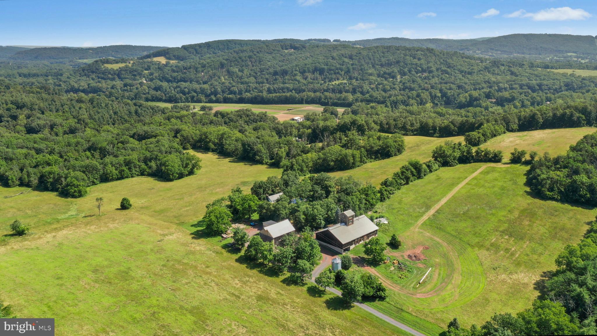 Set in the center of 90 UNPRESEVERED acres amongst fertile rural lands in an area seemingly untouched by modern time, Cairnson Farm, is one of a few pristine unaltered Bucks County farms that still remain and is available for the first time in approximately 50 years. Own everything you overlook…rolling pastures and mature forest for exploring and watching wildlife. Here a collection of buildings will spark dreams and opportunities. A circa 1800s home with wood floors and beamed ceiling rests in a setting that warrants restoration and expansion or use this home as a guest house and build a modern masterpiece on the highest point with long distance views of the majestic Delaware River.
A large barn building, previously used as a brewery, offers a versatile space for housing collections, equipment, projects and workspace. With a 4 story lookout, massive beams framing high ceilings and open spaces, concrete floors, electric, lighting and full bath, the cost to replicate this building would be considerable. An antique stone and frame bank barn is a classic piece of history and also offers room for equipment and collections.
With no restrictions the acreage is a refuge and a delight, offering a showcase of views and a symphony of silence where everyday, every season, presents a new opportunity to enjoy the pleasure of an unspoiled oasis in the middle of an oft too civilized world. Its country location is convenient to shopping, restaurants and entertainment and is the perfect weekend getaway from New York City and Philadelphia.
An adjacent c.1890s home on 3 acres is included and would be perfect for a caretaker, rental, or extended family. The interior of the home is as charming as the exterior featuring a living room with wood floors, decorative fireplace and beamed ceilings. A white eat-in kitchen with exposed beams and glass door overlooks the deck, lawns and forest beyond. Two bedrooms with wood floors and a bath with classic fixtures are found on the 2nd floor. A walk-up attic offers future expansion room. Steps away from the home a whimsical building is a bonus space with its wood floors, high ceilings with beams and abundant windows. This versatile building is perfect for a studio, workshop and office. A single car garage will accommodate a vehicle, toys and equipment. The abundant acreage is bucolic and offers a fenced vegetable garden, woodland to explore and plenty of area for pets and people to play.
