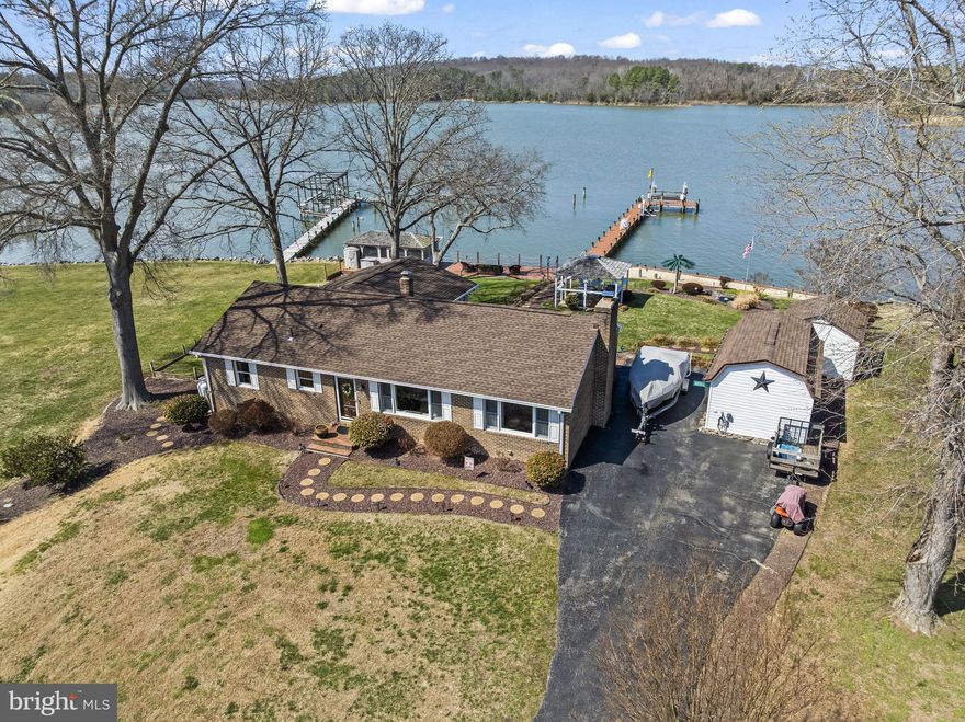 Entertainer’s Dream on the Water! This beautifully updated waterfront brick rambler in Golden Beach offers the perfect blend of relaxed coastal living and exceptional outdoor entertaining. The highlight of the property is the incredible backyard retreat featuring a 135-foot private pier with boat lift and jet ski lift, water and electric service, cable hookup, and 4–5 feet of mean low water—ideal for accommodating larger boats. Enjoy crabbing right from your dock, unwind on the private beach area, or entertain friends and family at the spectacular waterfront tiki bar complete with cathedral ceiling, custom bar with sink, icemaker, refrigerator, water heater, TV, surround sound speakers, and vibrant neon lighting that creates an unforgettable waterfront atmosphere. The outdoor space continues with a gazebo featuring a fireplace, gas grill, electric service, and ceiling fan, landscape lighting, multiple outdoor speakers, a large waterfront deck, and both wood and rock bulkheads for shoreline protection. Inside, the home offers a bright and inviting floor plan. The front door opens to a spacious living and dining area with hardwood floors, crown molding, chair rail, and decorative wainscoting, highlighted by a large picture window. The eat-in kitchen is beautifully upgraded with granite countertops, designer tile flooring and backsplash, recessed lighting, custom cabinetry with under-cabinet and accent lighting, a distinctive tin ceiling, and a professional Viking gas stove with pot filler. Stainless steel appliances include refrigerator, dishwasher, and built-in microwave. A pass-through connects the kitchen to the sunken family room featuring LPV flooring, knotty pine ceiling, recessed lighting, two ceiling fans, and a large picture window overlooking the water. The sunroom addition (approx. 21’ x 15’) is a standout feature with cathedral ceilings, propane gas fireplace with marble surround and wood mantel, surround sound, decorative window ledges, and two doors leading to the backyard oasis. The primary bedroom includes hardwood floors, crown molding, ceiling fan, private half bath, and direct access to the sunroom. A second bedroom also features hardwood floors, crown molding, ceiling fan, and water views. The renovated hall bath showcases a designer vanity with granite countertop, custom lighting and mirror, floor-to-ceiling tile walls, tile flooring, and a full tile tub/shower surround. Additional features include thermal windows approximately 10 years old, architectural shingle roof, encapsulated crawlspace, tankless water heater, water softener system (approx. 5–7 years old), whole-house generator already hardwired, and custom wood trim throughout. The extended driveway provides plenty of parking for a boat and multiple vehicles and also includes a Level 2 EV charging station (220V). There is pull-down attic access with floored storage space. Outdoor improvements also include two sheds—one finished with carpet, electricity, 220 outlet, and built-in workbench—plus a pond area and extensive lighting throughout the yard, dock, and bulkhead. Much of the furniture can convey, making this a rare opportunity to own a fully equipped waterfront lifestyle property designed for relaxing, entertaining, and enjoying the Chesapeake Bay lifestyle.