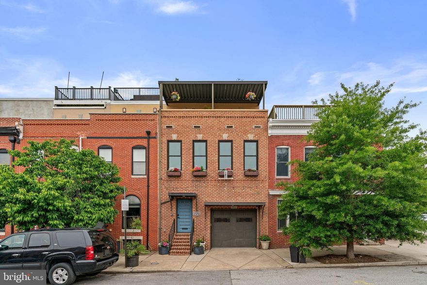 Stunning luxury row home in the heart of vibrant Canton offering an impressive 4,738 finished square feet, timeless Baltimore charm, and an unbeatable lifestyle just moments from the waterfront, acclaimed restaurants, boutique shopping, parks, nightlife, and major commuter routes. Showcasing classic city curb appeal with a striking brick façade and charming window garden planters, this remarkable residence also includes private parking—an incredibly rare and valuable amenity in Baltimore City.Step inside the welcoming foyer featuring ceramic tile flooring and a convenient coat closet before entering the expansive open-concept main living area. Rich hardwood floors flow throughout, complemented by exposed brick walls, elegant floating staircases, and a stylish powder room. The dining area seamlessly connects to the beautifully appointed eat-in kitchen, creating the perfect atmosphere for both everyday living and entertaining. The gourmet kitchen is thoughtfully designed with a spacious center island with bar seating, pendant lighting, abundant cabinetry, custom tile backsplash, and stainless steel appliances.Ascend to the next level where hardwood flooring continues throughout a spacious and sun-filled great room featuring a gas fireplace elegantly flanked by a built-in media center with storage cabinetry on one side and a sophisticated wet bar with a beverage refrigerator on the other. Extensive natural light, track and recessed lighting, chair railing accents, and additional exposed brick walls further enhance the inviting space. This level also includes a generously sized bedroom with an attached full bathroom featuring dual sinks, along with an additional powder room for guests.The expansive primary suite showcases a gas fireplace flanked by custom built-ins, a walk-in closet, a private covered veranda, and stylish barn doors opening to the spa-inspired ensuite bath with dual vanities and a striking glass block shower. An additional bedroom on this level features its own attached full bath and walk-in closet, while the conveniently located laundry room adds everyday practicality.The top-level loft offers exceptional versatility with a wet bar, refrigerator, powder room, and direct access to the spectacular rooftop deck (roof updated in 2023)—perfect for entertaining or relaxing while taking in sweeping Baltimore skyline views. The fully finished lower level provides an expansive recreation room ideal for a home gym, media room, lounge, or guest space, along with an additional full bathroom and utilities (HVAC updated in 2024).Exterior highlights include a garage equipped with a hydraulic lift and extra storage, a covered private veranda, an incredible rooftop deck overlooking the Baltimore city skyline, and a rear 1-car covered carport accessible through the alley.