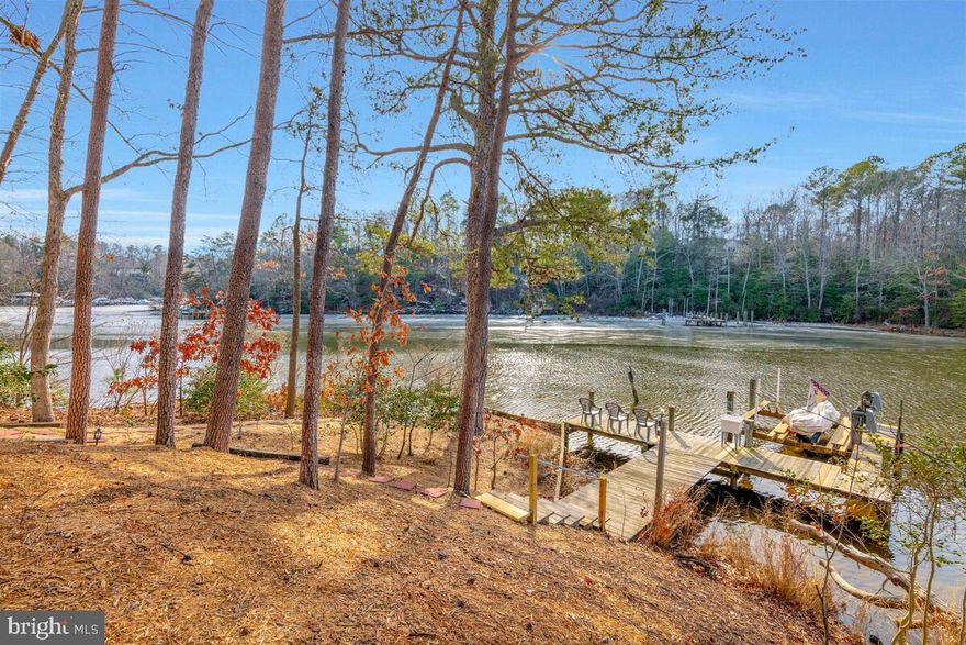 HUGE PRICE IMPROVEMENT!   A rare gem nestled on Mill Creek, this home offers tranquility and peace 365 days a year. As you relax in the stunning all-glass four-season room, you’re treated to a breathtaking 180° view of shimmering waters. It’s easy to see why this home is called “Glistening Waters.” As you walk down the gently sloping path to your private dock, complete with a 10,000-pound boat lift, electricity, water, and a sink for cleaning your catch of fish and crabs, the waters come alive with larger fish chasing schools of baitfish. After a day of water adventures, return to the expansive wraparound deck and unwind in your brand-new, covered hot tub, which features 92 jets and dual water purification systems to minimize the use of chemicals. The newly remodeled primary suite and bath offer serene water views through sliding glass doors that open directly to the deck and hot tub. Indulge in the luxurious spa shower system, complete with a heated towel rack for the ultimate in comfort and relaxation. The spacious, custom designed, walk-in closet provides ample storage, keeping your personal items organized and easily accessible. The primary suite is located on the main level, along with a cozy guest bedroom and a convenient half bath. The open-concept kitchen enjoys waterfront views and features high-end appliances, a walk-in pantry, washer and dryer, and an unused laundry tub hookup. The kitchen seamlessly flows into the living room, which is anchored by a gas fireplace, as is the primary bedroom, creating a warm, inviting atmosphere.  Downstairs, you’ll find two additional bedrooms, a full bath, and a kitchenette with another washer and dryer, a refrigerator, and ample cabinet space. The large living area offers plenty of space to relax or entertain. With three extra closets and a sizable workshop, the lower level of this nearly 4,000-square-foot home provides ample room for all your needs. A beautiful pellet stove heats the home, supplemented by central air and heat. Sliding glass doors lead to your private natural backyard, complete with a fire pit. Follow the deck path to extended seating areas, a stone dry river , and a charming wooden bridge. There are multiple spots to tie up a kayak, offering alternative water access if you prefer not to use the boat lift. The oversized two-car garage with extensive attic space provides plenty of storage and room for another workshop.  Location is key, and this home delivers. Situated closer to the water than neighboring properties, it offers exceptional privacy.   You’re just 5 minutes from museums and Solomons Island, and less than an hour’s drive to Washington, D.C. The home is also close to the Pax River Naval Base, offering easy access for those working in or near the base. Enjoy the best of both worlds: the peace and seclusion of a quiet dead-end street with only a few homes, while still having easy access to all the amenities of the Chesapeake Ranch Estates. Whether by boat or car, you’re only minutes away from Solomons, the beaches, and the Chesapeake Bay.  Call me today to schedule your private tour!