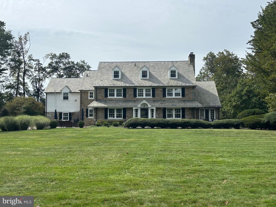 Step back to a time when location defined an estate's prestige. Set along Yardley’s storied Mansion Row in the heart of Delavue Manor, 2211 Yardley Road is a remarkable 1918 stone Colonial gracefully positioned on approximately 1.5 acres of beautifully curated grounds. This exceptional residence showcases enduring craftsmanship thoughtfully enhanced for modern living.
The stately stone exterior, slate roof, decorative columns, portico, dormers, and striking stone chimney create an unforgettable first impression, complemented by bluestone walkways that frame the approach. Inside, timeless architectural details abound, including rich hardwood floors throughout the first and second levels, extra-deep window sills, arched doorways, curved moldings, thick crown and chair rail moldings, 9-inch colonial baseboards, and classic Moravian tile accents. A gracious center hall entry anchors the formal living and dining rooms and features a grand staircase with a wide turned design and mahogany banister.
The formal dining room is a charming space for entertaining, centered by what is believed to be the home’s original crystal chandelier. A door leads to an expansive bluestone patio with seating areas framed by thoughtful plantings that provide privacy—perfect for outdoor dining or gathering with family and friends around the firepit on a crisp fall evening.
The grand living room offers generous proportions, custom built-ins, and a fireplace accented with Moravian tile, creating a warm and inviting atmosphere for both everyday living and holiday gatherings. Double French doors open to a luminous conservatory featuring exposed stone walls, Mercer/Moravian tile floors, surrounded in windows with multiple French doors leading to patios and gardens beyond. Bathed in natural light, this exceptional space is the perfect setting to relax with a book or simply enjoy the surrounding landscape.
The thoughtfully designed kitchen blends period charm with modern functionality, offering glass-front cabinetry, newer stainless-steel appliances, stone countertops, and generous preparation space. The open layout enhances flow for both daily living and entertaining. A butler’s pantry with additional cabinetry, farmhouse sink,  dishwasher, beverage fridge and extra oven provides exceptional storage and convenience. A charming powder room accented with Moravian tile completes the main level.
The second floor features four bedrooms and three full baths, including a spacious primary suite with deep window sills, built-in cabinetry, and a generous walk-in closet. The beautifully remodeled primary bath showcases a walk in shower with frameless door and a double vanity with stone countertop. Two tastefully updated baths serve the remaining bedrooms, while a separate back staircase connects the former maid’s quarters to the main floor. The third floor provides two additional bedrooms that share a large full bath featuring classic Moravian tile. Perfect for guests, a home office or creative pursuits. 
The finished lower level expands the home’s living space with an inviting entertainment retreat complete with a bar, billiards area, comfortable seating space, full laundry room, and abundant storage.
Outdoors, the grounds feel like a private garden retreat with expansive lawns, raised garden beds, mature perennials, peonies, blueberry bushes, herbs, and fruit-bearing plantings. Multiple patios and a firepit create wonderful spaces for relaxing or entertaining. An attached two-car garage and dual driveways with a turnaround provide everyday convenience.
Ideally located just minutes from downtown Yardley’s shops and dining, the scenic Delaware River, the train to Philadelphia and New York, major commuting routes, Princeton, and local township recreation, this exceptional home offers a rare blend of architectural heritage, gracious scale, and modern comfort in one of Lower Makefield Township’s most coveted settings.