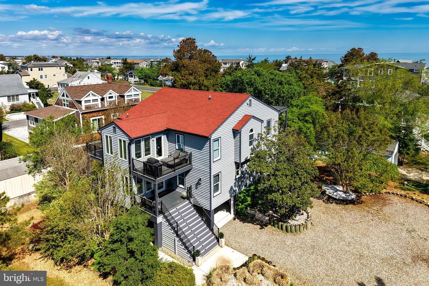 ONE-OF-A-KIND IN LEWES BEACH and perfect in every way: lot, location, and luxury upgrades.  Set on an oversized lot, this exceptional home offers a rare combination of space, privacy, and resort-style amenities. The expansive front area provides private off-street parking for up to eight vehicles or ample room for outdoor recreation such as cornhole, badminton, bocce ball, horseshoes, private parties, and more.  Ideally located close to everything Lewes has to offer, the home is just minutes from the beach, restaurants, downtown Lewes, the ferry terminal, Cape Henlopen State Park, bike and walking paths, and access to the Lewes-Rehoboth canal.  Since 2022, this property has been a highly successful vacation rental and is offered fully furnished with high-end finishes throughout. Recent upgrades include a professionally installed hydrotherapy hot tub , a new roof, and two new mini-split systems.
The home is equipped with five sleeping areas, including four bedrooms—one with a king bed and three with queen beds—plus a spacious family room featuring two sets of bunk beds. There are two full bathrooms with glass-enclosed showers, a powder room, and a seasonal shower room on the ground level.
Designed as an inverted home to maximize light and views, the third floor features a stunning open-concept living space with two balconies on one side, and a deck on the other side. Highlights include a large kitchen with a U-shaped counter seating eight and a wine refrigerator; a dining area with seating for ten; and a living area anchored by a modern linear gas fireplace that creates a warm, inviting ambiance. This level also includes two bedrooms (one king, one queen), a full Jack-and-Jill bathroom, a half bath, and a tranquil ZEN Room with beautiful views of marshland and Lewes proper.  The second level houses the family room with bunk beds, a side entry leading to a deck and staircase with elevator access, two queen bedrooms connected by a Jack-and-Jill bathroom, a private office, a cozy reading nook with walk-out balcony and front deck, a lockable owner’s closet housing the water heater, and an adjacent coat closet with the AC unit. The private office is accessible both from outside and through one of the bedrooms, offering flexibility for work or quiet retreat.  The ground level offers multiple inviting spaces to relax and entertain, including a covered porch with outdoor TV, sink, bar area and ping-pong table; a cabana for beach gear with a full-size refrigerator/freezer with a seasonal water and ice dispenser; al fresco dining area; a secluded “secret” patio; a fenced backyard with a fire-pit and comfortable Adirondack chairs; a hot tub area with an adjacent seasonal shower room; a private gym; an outdoor freight elevator with access to all three levels of the home; and additional lockable under-stair storage for bikes. The thoughtfully designed outdoor landscape is low maintenance and features an irrigation system, pollinator garden, Japanese garden, herb garden, and a beautiful covered walkway with pergola. Welcome home!