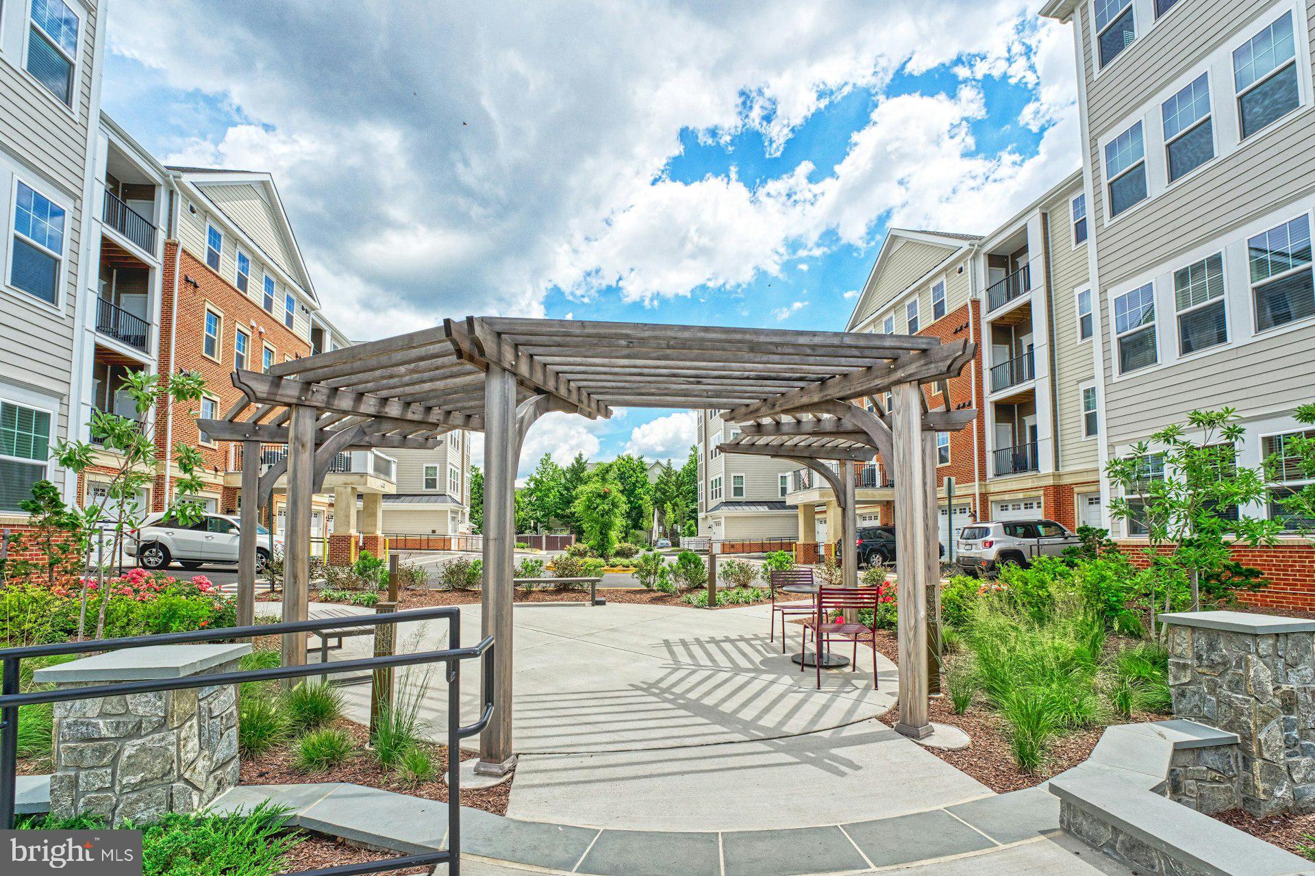 Step into the pinnacle of refined living with this impeccably designed Chestnut model penthouse—an exclusive top-floor end-unit in one of Northern Virginia’s most desirable 55+ luxury communities. Soaring 10.5-foot ceilings and expansive windows fill the space with natural light, creating an airy, elegant ambiance that feels both sophisticated and inviting. Every detail has been thoughtfully curated to surpass even the builder’s model, offering a seamless blend of comfort, style, and elevated finishes. The open-concept floor plan flows effortlessly, making it ideal for both quiet enjoyment and entertaining in grand fashion. The chef’s kitchen is a standout, featuring premium KitchenAid appliances including an induction range, sleek cabinetry, designer fixtures, and refined surfaces that make culinary pursuits a pleasure.
The primary suite serves as a private retreat, enhanced with custom plantation shutters, a spacious layout, and a spa-inspired bath designed for relaxation. A second bedroom provides flexibility for guests, an office, or creative pursuits, while both bathrooms are appointed with tasteful finishes that complement the home’s luxurious feel. A private balcony offers the perfect setting for morning coffee or sunset toasts, providing a peaceful outdoor escape. Additional conveniences include a private one-car garage equipped with a 220V EV charging outlet, direct secure access to the building, Energy-Star certification, and a Broan Fresh Air Filtration System to ensure a healthy living environment.
Ideally situated just a short stroll from upscale shopping, dining, and local amenities, this penthouse offers the ultimate in low-maintenance, lock-and-leave living. Protected by 1-year, 2-year, and 10-year builder warranties, the home provides peace of mind alongside its impeccable style. This is a rare opportunity to experience luxury, ease, and vibrant community living—all from the comfort of a penthouse that truly sets a new standard