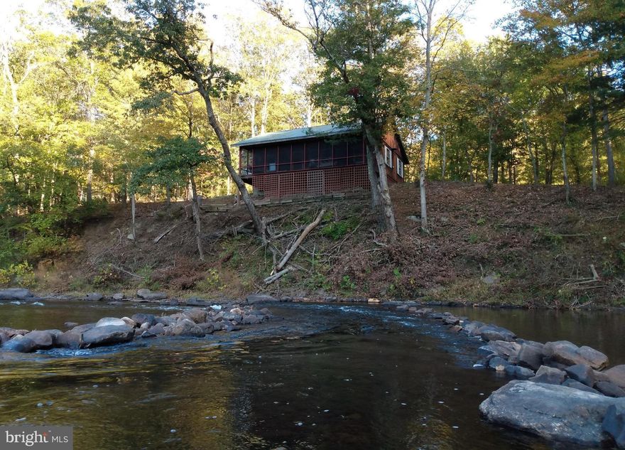 Cacapon River! over 250 ' of Sparkling River frontage, this cabin sits only feet from the edge but certified high and dry! This is the prettiest location you will find on the creek, and you will enjoy the easy access to the river's edge and beach like setting that it offers. The cabin was quality built in 1964 and has that nostalgic charm, knotty pine interior walls, a solid brick wood burning fireplace, some of the pine plank floor is exposed. A full-length screened in porch overlooks the water with the incredible sounds of the ripples making their way to the porch and a very large wooden swing that's perfect for taking a nap. 3 bedrooms, 1/2 bath with a separate shower room, open living room / kitchen design and a bonus room above. Newer green metal roof.  Furnishings convey making this cabin ready to enjoy now. This is truly a rare find for anyone that's been searching for a riverfront weekend retreat.