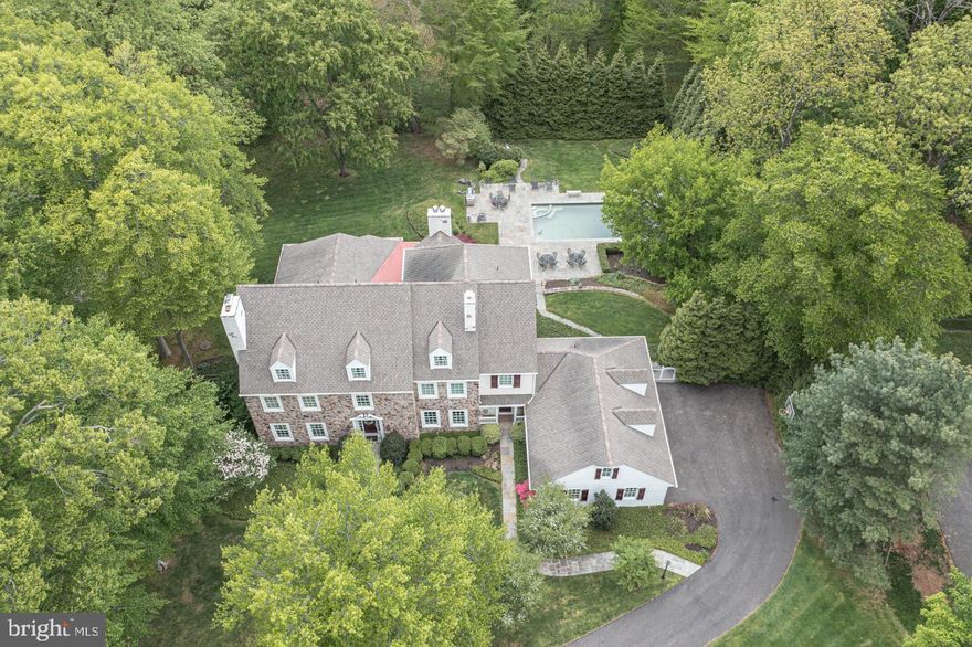 Welcome to 18 Timber Knoll Drive, a charming Bucks County reproduction manor home nestled on almost 2 acres in historic Washington Crossing. Featuring 6 bedrooms and 5.5 baths displaying notable stately architectural details throughout including intricate moldings, wainscoting, columns, coffered ceilings and true divided-light multi-pane windows.  The prominent stone front exterior with dual front entry and flagstone walkway is as timeless and classic as the interior. The inviting 6,700 square foot floor plan and arched entry ways lend to endless allure around every turn of this home. Upon entry, you will find a striking centrally positioned curved staircase and a nearby intimate and spectacularly designed library with walls of impressive floor-to-ceiling custom, built-in bookshelves, anchored by a stunning gas fireplace showcasing Mercer tiles. Across the foyer, the front living room is spacious and features a useful double-sided wet bar concealed by paneled doors, a second gas fireplace, this one fashioned with a marble surround, and a seamless flow into the naturally lite formal dining space with its wall of paned windows, eye-catching tray ceiling, two corner built-ins, wainscoting, and kitchen access. The open floor plan showcases a generously sized great room that streams easily into the grand gourmet kitchen, thoughtfully outfitted with high end appliances, granite island and countertops with seating for 8 bar chairs, and the lengthened coffered ceiling solarium breakfast room, lined with expanded built-in banquette seating/underneath storage accommodating 50+ sit down guests and pleasing space for your hosting needs.  Just off the kitchen, the cozy covered white railing and column accented veranda with its Southern style charm and ambience suggests a welcoming spot of shade and comfort during the warm summer months along with picturesque views of the park-like setting backyard and glimmering pond. The inviting, yet elegant great room with stone fireplace, is drenched with sunlight from the multiple arched transom highlighted windows and allows for scenic views of the private wooded backdrop, several bluestone patios and pool with built in hot tub. A large suite found on the opposite side of the main level can be utilized as a main floor guest suite or perhaps in-law quarters. Completing this level is a powder room, convenient mudroom with storage and back staircase. Upstairs, in the owner's suite, you will find a bright, light-filled bedroom with plenty of space, fireplace, 2 walk-in closets, and a calming en-suite bathroom with jetted soaking tub, dual vanities and walk-in steam shower. Accessed via the owner’s suite or hall, offering wonderful versality, is a nursery/bedroom. The upper level also encompasses a roomy office, princess suite with a newly updated bath, and 2 bedrooms sharing a newly updated full hall bath. Make your way down the wainscoted staircase to the fully finished, expansive walk-out lower level offering amazing multiple entertainment areas including a game space, media area with stone fireplace and full wet bar, wine cellar with 800 bottle wine refrigerator, workout room with cedar dry or steam rock sauna, and steam showered bath with changing room and thoughtfully built-in storage cabinetry for pool guests. Walk out through French doors to a beautiful bluestone patio featuring multiple sitting areas, stone seating walls, lush landscaping and meandering walkways leading to the sparkling pool. This home has been meticulously updated and maintained and offers so many thoughtful selections. Additional amenities include an upstairs laundry room, downstairs workshop, spacious 3-car garage, open staircase leading to a third story three-dormered attic with 8-foot ceilings, plumbing and electric roughed in for additional living space. Located in the Council Rock School District, close to both Newtown and New Hope for shopping, entertainment, dining, and convenient to the I-295 corridor.