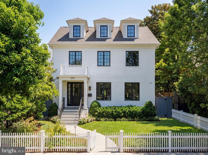 Set against the iconic backdrop of the National Cathedral in the heart of verdant Cathedral Heights, 3117 38th Street NW is a masterfully crafted modern farmhouse designed by GTM Architects in collaboration with MMg Development and built by Murillo/Malnati Homes. This distinguished team partnered with acclaimed landscape designer Lila Fendrick to deliver a residence that marries high design with luxurious livability, showcasing top-tier craftsmanship, seamless indoor-outdoor flow, and enduring style.

Completed in 2019, the home spans nearly 8,000 finished square feet across four thoughtfully designed levels. A white brick façade, black-trimmed windows, flagstone walkways, and manicured landscaping create timeless curb appeal. The front portico opens to a gracious foyer with sightlines that extend to the rear terrace, setting a tone of openness and elegance. Crown moldings, gleaming hardwood floors, and abundant natural light provide a sophisticated yet welcoming atmosphere.

The formal living room, with a gas fireplace and custom built-ins, overlooks the front garden. A tray ceiling and wainscoting in the adjacent dining room elevate formal gatherings. A marble-clad butler’s pantry with a beverage fridge connects seamlessly to the chef’s kitchen, which features custom stacked cabinetry, Wolf and Sub-Zero appliances, a full-height marble herringbone backsplash, and an expansive island with bar seating.

The open-concept kitchen and adjoining family room serve as the heart of the home. Coffered ceilings, a marble fireplace, and dual sets of French doors open to a flagstone terrace beneath a full-width pergola, perfect for indoor-outdoor entertaining and framed by views of the Cathedral.
Additional main-level features include a custom mudroom with built-in cubbies and side entry, access to a detached two-car garage with EV hookup, and a large walk-in pantry. A powder room and elevator complete this level.

Upstairs, the primary suite occupies its own wing and includes a private rear deck with cathedral views. The spa-inspired primary bath features radiant heated marble floors, a freestanding soaking tub, a glass-enclosed shower, a wall-spanning double vanity, and a private water closet. A custom dressing room with golden backlit shelving and abundant storage completes the suite. Three additional bedrooms, one currently used as a home office, share two full bathrooms along with a large, fully equipped laundry room.

The third level offers flexible living with two additional bedrooms, one styled as a game room with alcove seating, and a full bath. This space is ideal for guests, teens, or creative pursuits.

The finished lower level includes high ceilings, a recreation room with integrated Sonos sound, a wet bar with a Sub-Zero beverage fridge, a custom wine room, a fitness studio, a powder room, and a second laundry area. A private guest or au pair suite features a kitchenette, bedroom, and full bath.

Smart home systems include Legrand lighting, Honeywell Pro Series thermostats, integrated security with cameras and motion sensors, and multiple wall-mounted iPads for controlling lighting, sound, and surveillance.

Outdoors, a flat, professionally landscaped lawn is pool-ready and features a built-in grilling station, an extensive stone terrace, ambient lighting, irrigation, and French drainage systems for year-round enjoyment.
Steps from Massachusetts and Wisconsin Avenues, this premier location offers proximity to top-rated schools, lush parkland, and downtown DC. Elegant yet approachable, richly appointed yet supremely functional, 3117 38th Street NW is a rare offering that defines modern luxury living in Washington.