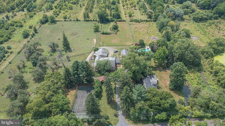 If you want to immerse yourself in Bucks County life surrounded by fresh air, countryside fields and farmland, Mill Creek Farm, a wonderful farmstead has what you are looking for and more! Nicely nestled on 14+ scenic acres, this circa 1730s historic property, once a quaint B&B, offers endless amenities beginning with an original stone manor, 13-stable horse barn, summer kitchen, corn crib, tennis court, pool with hot tub and a pond. Over the years the barn has been converted and renovated into 5 income producing apartments yet still keeping the horse stables intact along with two birthing areas that were used to breed thoroughbreds, making it very much a working farm in its day. The main house includes 5 bedrooms, 5 full baths and a convenient half bath. The rooms are comfortable with period dated hardware, deep windowsills, exposed ceiling beams and exposed stone walls. A favorite space in the manor is the enclosed porch adorn with bar and several sitting areas overlooking the Lahaska Creek flowing through the back of the property where you can rest in front of the stone fireplace and enjoy the picturesque views. At night you can step outside for backyard fireside chats by the creek and see a full sky of stars while listening to the sounds of nature or relax in the other delightful outdoor living areas such as the cozy spot by the summer kitchen known as The Crape Myrtle Pub with bar offering indoor and outdoor seating.  A bonus find on the third floor are the rare high ceilings and two private bedrooms with bonus storage. Perfect for a family compound and/or equestrian enthusiast this farm is situated about a mile away from town; along a quiet country road - Quarry Road, named after a quarry that used to exist a long time back at the end of the road which supplied the stone that gives the distinctive style to the buildings in the area. Overlooking green pastures, apple orchards, a pond and acres of serene gardens yet convenient to many Bucks County attractions and close to Doylestown, Lahaska’s Peddlers Village, and New Hope with its assortment of eateries and shops. Experience the peaceful grounds of this horse farm where William Penn held the farm’s first deed and immerse yourself in the country scenery and you’re sure to fall in love with this unique property!