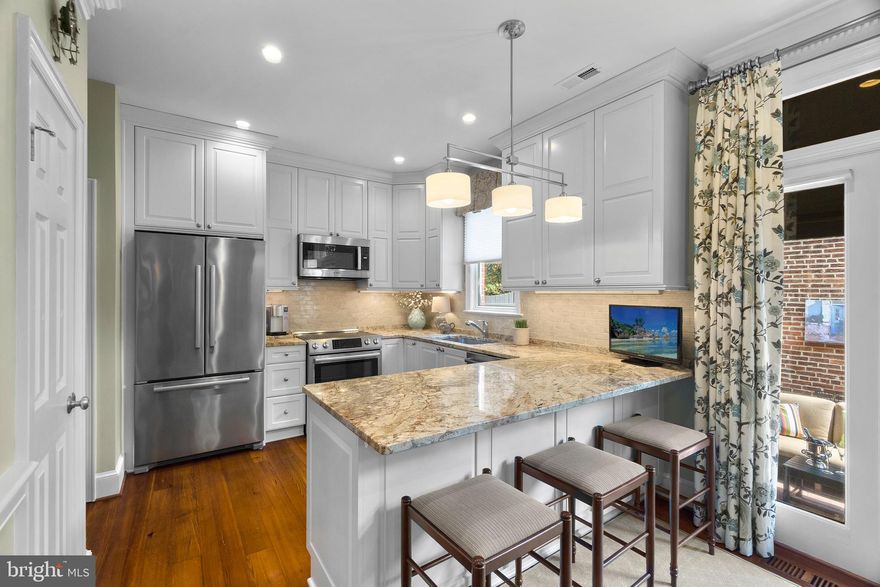 Do you dream of a nicely upgraded, beautifully appointed TH located in the heart of Old Town Alexandria, with off-street parking, a front entrance without cars parked 10 feet from your front door, and a private brick courtyard to enjoy as your home? Welcome to 314 S. Columbus St, a 3 bedroom and 3 full/1 half bath TH, with 2420 finished sq.ft. on four levels and an all-brick exterior. The quality of the fit and finishes chosen is evident throughout the house. The same applies to the level of care and maintenance given to the home. House Details: The visual appeal of this house starts as you walk along the landscaped brick walk to the Portico entry and the Colonial red front door with all Baldwin brass accents. The house opens to the Living Room with a fireplace and flanking built-in bookcases as the focal point of this space. Plantation shutters on the windows provide both visual appeal and the desired amount of Natural light.
The Living Room leads to the fully remodeled kitchen, with Bosch appliances and seating at the peninsula counter. The kitchen offers space for a separate dining table with banquette and chair seating.
The kitchen overlooks the enclosed brick patio, which is accessed via the French door with transom and side windows providing added natural light. Privacy is provided by a 2-story brick wall opposite the kitchen, which also provides a nice visual background to view from inside the house. An oversized, retractable awning (motorized) also adds to the privacy and intimacy of this outdoor space.
Reclaimed Heart Pine flooring from a mill in Maine adds a rich warmth to the Main Level.  Along with a sense of History. A fully updated half bath is also located on the Main Level. The second floor has the Owner’s Suite bedroom, with Plantation shutters on the two windows. Another fireplace and flanking built-ins provide both a design focal point and additional storage. The Owner’s Suite has two (His & Hers) fully remodeled full bathrooms, which the same quality finishes and attention to details as found in kitchen. The Owner’s Suite also has three closets for storage. The 3rd floor has two additional bedrooms, an updated 3rd full bath, & the laundry . The top two floors also have Heart Pine flooring. The lower level has a finished space with carpeted flooring that is large enough for oversized, comfortable seating and bookcases to create an Owner’s Retreat space for a quiet read. Or to enjoy your favorite sporting event. This level also has a large, walk-in mechanical room with a high ceiling and storage shelving. The TH has a central vacuum system. The HVAC systems are Trane units (2020 & 2008 installation), with annual Spring/Fall maintenance since installation. The water heater was installed in December 2019. The house has vinyl-clad, double-hung replacement windows throughout. The roof is the responsibility of the Association. The TH has two assigned parking spaces in the parking lot beside the building. 314 S. Columbus is located one block from Duke and S. Washington Streets, so the location is truly in the heart of Old Town Alexandria, withing walking distance to…Everything. Like King Street shopping? The TH is located just two blocks from Patina Polished Living and Manse, with Red Barn Mercantile a 10-min walk from the front door. Like Old Town dining? All of your favorite Old Town restaurants are within a 15-min walk from front door. For example, Josephine on S. St. Asaph is a 7-min walk. Like dining or a stroll along the Potomac Waterfront? Virtue Feed & Grain, Blackwall Hitch, Vola’s, Barca, and Ada’s are a 15-min walk. Like Old Town History? The Lyceum (Alexandria History Museum) is a 4-min walk. The Old Town Farmers Market at City Hall is the oldest continually operated Farmers Market in the County (open Sat year-round 7am-Noon). The Market is a 10-min walk. Check out the “A Stroll through Old Town Alexandria" video about living in the Heart of Old Town on the virtual tour.