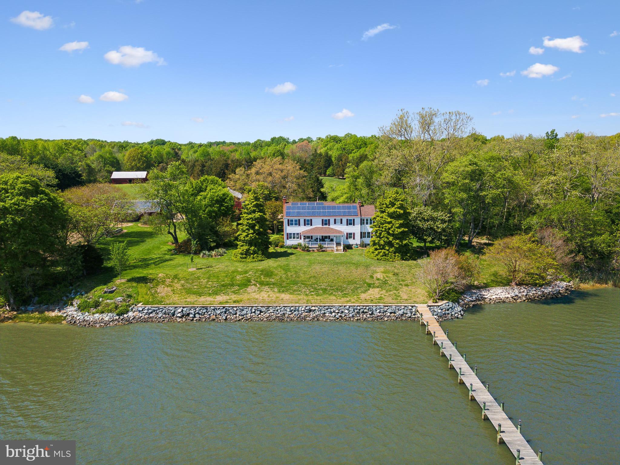 Welcome to 9310 Tayloes Neck Road, a breathtaking waterfront farm nestled in the tranquil surroundings of Nanjemoy, MD. This remarkable property offers the perfect blend of serenity and accessibility, just a convenient commute from the vibrant heart of Washington, DC and across the river from Quantico, VA. Spanning approximately 3,000 square ft., the home features four bedrooms and three well appointed bathrooms, providing ample space for comfort and relaxation. An enclosed porch welcomes you into the home, while a covered porch in the back facing the waterfront provides a magnificent view of the Nanjemoy Creek as it opens up to the Potomac.
Set on over 12 sprawling acres, this unique estate presents an array of opportunities for both leisure and productivity. The property includes a spacious dock, perfect for boating adventures, soaking in the picturesque views of the water, or casting a fishing line. The surrounding land includes a well-equipped barn offering versatile usage. Outside the barn are vegetable patches, a chicken coop and a fenced-in grazing area with an additional outbuilding. Embrace sustainable living with electricity generated from state-of-the-art solar panels, reflecting a commitment to eco-friendly practices.
The expansive lot invites endless possibilities—whether you envision cultivating a flourishing farm, enjoying recreational activities, or simply basking in the tranquility of the natural surroundings. The lush landscape and waterfront views provide an idyllic retreat, making this property a rare gem for those seeking a harmonious blend of nature and convenience. Experience the best of both worlds at this extraordinary Nanjemoy estate.