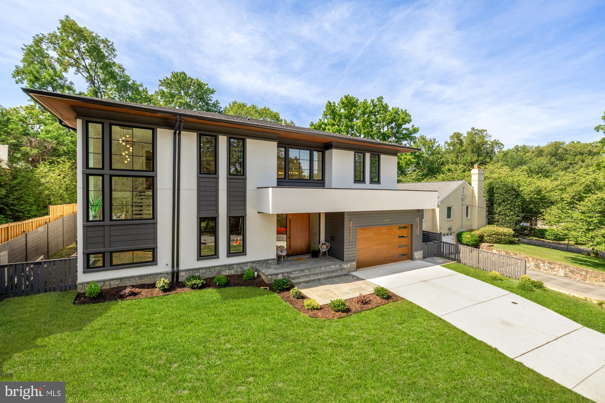A Striking Blend of Timeless Design and Modern Sophistication
6018 Madawaska Rd is a meticulously crafted contemporary residence, nestled in the desirable Glen Echo Heights enclave of Bethesda, within the coveted Whitman/Pyle school cluster. Thoughtfully designed to meet the demands of modern living, this exceptional home offers today’s most sought-after conveniences—including an open-concept layout, en-suite baths, generous closets, a private elevator, bedroom-level laundry, and an attached two-car garage.
Far from a typical new build, this stunning home is a showcase of quality, creativity, and craftsmanship. Every inch of the home has been meticulously curated by a seasoned Builder who is also a distinguished local Interior Designer. From the tile to the lighting, each finish and fixture has been hand-selected to create a one-of-a-kind living experience defined by elegance and enduring style.
From the moment you arrive, the home exudes a sense of understated luxury with its refined Stucco and Boral Dutch Cove exterior and a handcrafted White Oak pivot front door that makes a bold and elegant first impression.
Inside, floating white oak stairs, designer light fixtures, and wide-plank white oak hardwood floors set the tone for a home that is as visually stunning as it is functional. Designed for both grand entertaining and comfortable daily living, the main level features soaring ceilings, light-filled formal spaces, and a striking aesthetic grounded in refined materials and architectural harmony.
The main level features a welcoming foyer with herringbone patterned flooring, a gracious sitting room with a slat wood wall accent in red maple, a gourmet kitchen with walk-in pantry, formal dining, a stylish powder room, laundry room, mudroom, and an expansive living room anchored by a sleek gas fireplace. The chef’s kitchen is outfitted with top-of-the-line Thermador appliances—including a microwave drawer insert hood with airflow control, a French door refrigerator—alongside a Porcelanosa tile backsplash, under-cabinet lighting, Calacatta Grigio countertops, a Blanco sink, and custom three toned cabinetry by David Bradley in collaboration with Montgomery Kitchen & Bath. A large mitered-edge Calacatta quartz island crowned by Parisienne-glam pendant lighting completes the space.
Ascend the floating staircase with custom glass panel to the upper level, where you'll find five generously sized bedrooms, each with its own bath, and a versatile lounge area. The show-stopping Owner’s Suite boasts a tray ceiling, custom accent wall, dual walk-in closets, and a spa-inspired bath with tray ceiling, bespoke wallpaper, Porcelanosa tile, freestanding tub, curbless stand up shower with frameless glass door, bidet toilet, mid-century modern dual vanity by James Martin, and dedicated laundry for added convenience.
The fully finished lower level offers an expansive recreation space with Luxury Vinyl Plank flooring, a second gas fireplace flanked by custom built-ins, striking designer wallpaper, a wine cellar, wet bar, and beverage station—perfect for entertaining or unwinding. This level also features a sixth bedroom and sixth full bath ideal for guests, an au pair or the in-laws.
An expansive accordion door on the main level opens to a private, level backyard retreat—complete with a patio and built-in natural gas grill—ideal for seamless indoor-outdoor living. Access to the rear grounds is available from the lower level for added convenience.
Additional highlights include a custom elevator servicing all three levels—ideal for multigenerational living—custom architectural windows, 25-year architectural asphalt shingles, and dual-zone HVAC for year-round comfort.