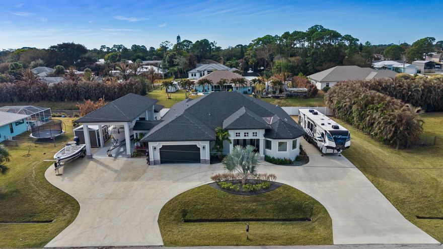 From the moment you step inside, this custom home makes a statement of understated luxury and exceptional craftsmanship. Soaring 10-foot ceilings and signature double-coffered ceilings with crown molding create an elegant architectural presence, while the open layout feels both expansive and inviting. The heart of the home is a beautifully designed kitchen featuring granite surfaces, stainless steel appliances, modern statement lighting, recessed and under-cabinet illumination—an ideal setting for both elevated entertaining and everyday living. Light pours through impact-resistant windows, enhancing the home's refined finishes and thoughtful details throughout the main living areas. The primary suite is a true private retreat, offering a striking double-coffered ceiling and generous his-and-hers walk-in closets. The spa-inspired primary bath elevates the experience with a luxury, double-sided walk-in shower featuring dual shower heads, designed for both comfort and indulgence. And then-freedom. NO HOA. Bring your boat, RV, and all your toys. With a circular driveway, dedicated RV pad, boat parking, detached carport, and detached air-conditioned garage/workshop, this property delivers the space and flexibility rarely found in custom homes of this caliber. A meticulously crafted residence offering luxury, privacy, and lifestyle freedom-all in Port St. Lucie.