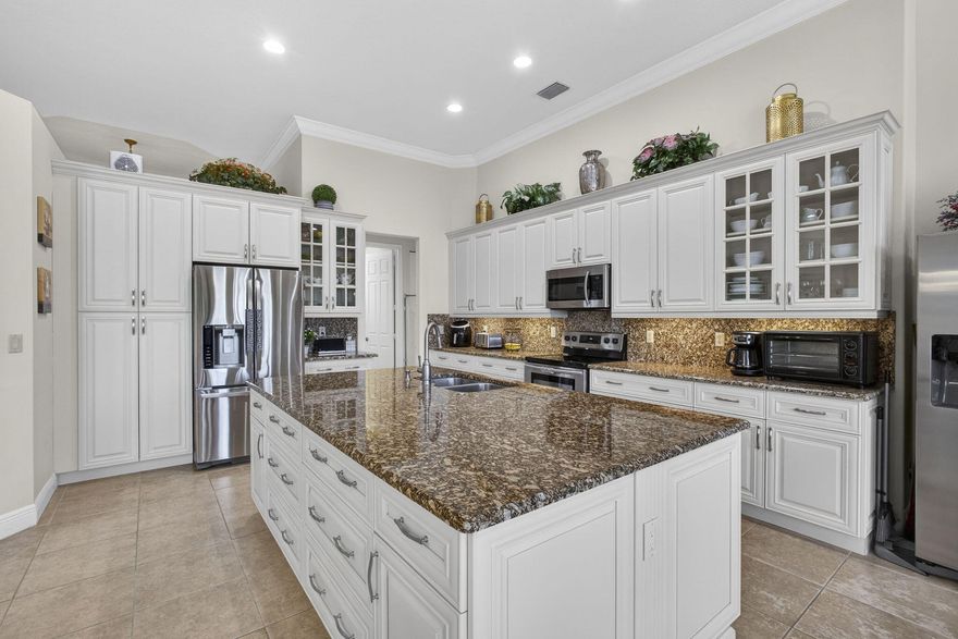 Wake up to breathtaking lake and rolling golf course views in this expansive 4-bedroom+den/5th bedroom, 3-bathroom, 3-car garage residence located within the gated, resort-style community of Palm Estates at Madison Green. Designed with soaring 12-foot ceilings, elegant crown molding, and an abundance of natural light, this home offers a blend of openness, sophistication, and tranquility. From the moment you step through the grand double-door entry, uninterrupted views through the living space to the sparkling lake create an impressive first impression. The interiors are bright and airy, with soft natural earth tones that enhance the light-filled spaces. Nearly every window has picturesque views of rolling greens, peaceful water, and Florida wildlife, bringing the outdoors beautifully into everyday living.  At the heart of the home is a fully remodeled chef's kitchen designed for both function and style. Featuring 42-inch upgraded white cabinetry, granite countertops, stainless steel appliances, and thoughtfully designed pull-out drawers for effortless organization, the space is elevated by soaring ceilings that add to its grand presence. A massive center island anchors the room, making it ideal for entertaining, casual dining, or gathering with family and friends.

The split floor plan offers privacy and flexibility. The primary suite is privately positioned on its own wing, encompassing dual walk-in closets, direct patio access, and a spacious spa-inspired bathroom complete with a jacuzzi soaking tub and separate shower. A dedicated office provides the option of a fifth bedroom, while a separate wing offers in-law potential with a private entry opportunity, perfect for multigenerational living or additional income possibilities.

Outdoor living is exceptional. The expansive 1,150-square-foot fully screened patio serves as an extension of the home, creating the perfect setting for morning coffee at sunrise, evening gatherings, or simply relaxing while overlooking the serene lake and manicured golf course. The oversized backyard and corner positioning provide additional privacy and space rarely found within the community.

Additional highlights include a durable 40-year cement barrel roof, new carpeting in the rear bedroom, a new silent garage door opener, full set of cabinets in the garage that could be used as a second kitchen, and a screened pre-entry vestibule that adds convenience, security, and protection for your packages. With one of the lowest HOA fees in the area at just $262 per month, residents enjoy gated living, walking trails throughout, and a top rated public golf course. True resort-style living at its best.
Living at 2626 Arbor Lane means enjoying all that the highly desirable Madison Green community has to offer. This gated, resort-style neighborhood is known for its exceptional amenities, including a stylish clubhouse, Olympic-sized heated pool and spa, kids' pool and playground, fitness center, lighted tennis and basketball courts, and scenic walking trails -- all designed to support an active, social, family-oriented lifestyle. Residents also appreciate the adjacent non-equity Links at Madison Green golf course, public and accessible without membership, offering world-class play and unparalleled views. Positioned just minutes from top-rated schools, premier shopping, diverse dining options, major highways, and the Florida Turnpike, Madison Green combines convenience with community charm. Whether you're commuting to work, exploring nearby parks, or enjoying local attractions, this location delivers the perfect balance of tranquility and accessibility in the heart of Royal Palm Beach.