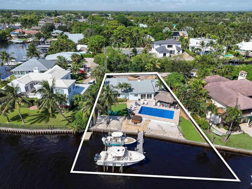 An exceptional opportunity to build your own 8,600 sq ft waterfront masterpiece on one of the most desirable stretches of the Loxahatchee River—see builder floorplan for what's possible on this incredible lot. In the meantime, enjoy a stunning waterfront oasis that delivers the ultimate Florida boating lifestyle. A true boater's paradise, the property offers direct intracoastal access with no fixed bridges, just minutes to the inlet, and features two boat lifts (6,000 lb and 12,000 lb) plus a private dock. Resort-style outdoor living awaits with a recently resurfaced saltwater heated pool, lush tropical landscaping, a Tiki hut with TV, and your own private sandy beach area. Inside, the home showcases 10-foot ceilings, tongue-and-groove accents, and an updated kitchen that blends coastal charm with modern convenience. A new roof and full storm protection provide year-round peace of mind. Additional highlights include a circular driveway, generous indoor and outdoor living spaces, and sweeping water views from nearly every room.  Whether you choose to enjoy this charming waterfront home as-is or create a custom luxury estate, this property offers a rare combination of location, lifestyle, and limitless potential on the scenic Loxahatchee River.
