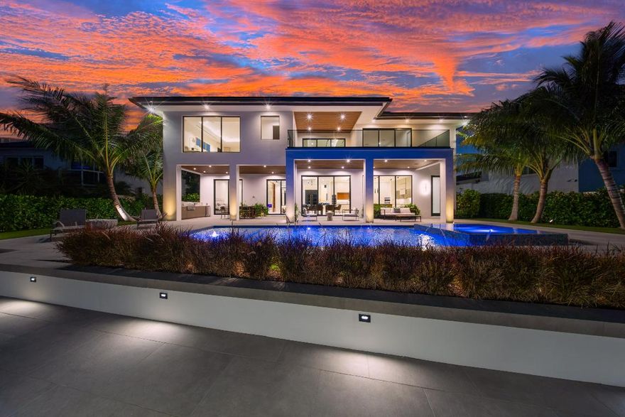 A modern masterpiece sited on the main intracoastal offering unrestricted saltwater and seamless direct ocean access. This estate seamlessly blends sleek architectural design, luxurious amenities, and cutting-edge technology to offer an exceptional South Florida lifestyle. Nestled minutes from Hillsboro and Boca Inlets, this waterfront home is ideal for yachting enthusiasts with its 91-foot yacht dock complete with bumpers, cleats, Shore Power Pedestal, and water supply, all secured by robust concrete pilings and evening lighting. The home's custom architectural design is captivating, combining tropical landscaping with expansive 10-foot PGT impact glass doors that welcome natural light while connecting indoor and outdoor spaces. An entertainer's paradise, the exterior offers a spacious loggia with a summer kitchen, a gas-powered concrete fire bowl for ambiance, and a saltwater pool and spa with sun shelves, LED bubblers, a spillway, and powerful jets all controlled by the smart home automation system. The second-story covered balcony is thoughtfully equipped with cable railings, water spigots, and a smart home interface. Inside, 12-foot ceilings enhance the sense of grandeur, while panoramic water views set the tone for the open floor plan. Sophisticated finishes like European oak engineered hardwood and expansive 48x48 porcelain tiles grace the living spaces, anchored by a water vapor LED-lit fireplace in the formal living area. A custom LED-lit staircase with glass railings and wood capping serves as a stunning architectural feature in the bright, welcoming foyer. The gourmet kitchen is a culinary dream, complete with leathered Taj Mahal quartz countertops, and high-end Monogram and Bosch appliances, including dual built-in refrigerators, a Bosch espresso machine, and a Thermador wine fridge. A jumbo-sized island provides ample seating and prep space, while a central vacuum with toe-kick features keeps the kitchen spotless. The butler's pantry, trimless recessed lighting, and dedicated office space with glass doors and custom cabinetry add both functionality and style. The primary suite is a sanctuary, boasting waterway views from a private terrace, a custom breakfast bar, his-and-her vanities, an elegant makeup vanity, and expansive walk-in closets. The oversized shower, designed as a spa-like retreat, includes dual rain heads, body jets, and floating benches. A mother-in-law suite on the main floor offers privacy and comfort, with easy access to the pool, dock, and outdoor shower via a cabana bath. Equipped with advanced smart home and security systems, the property features a Ring doorbell, four CCTV cameras, motion-sensor flood lights, and comprehensive automation that controls lighting, climate, pool, and security. Energy-efficient features include Low-E glass, tankless water heaters, R-20 foam insulation, gas lines for essential appliances, and a generator-ready setup for added reliability. A two-zone 17 SEER HVAC system ensures optimal temperature control, while a 600 AMP underground electrical service and Cat-6 wiring throughout the home keep it future-ready.  Adding convenience, dual laundry rooms, a mudroom with custom storage, and an oversized three-car garage with car lift compatibility, utility sink, central vacuum, and side-mounted motor provide ample functionality. Thoughtfully designed down to the last detail, a private waterfront oasis offering elegance and cutting-edge technology, for a truly luxurious lifestyle.