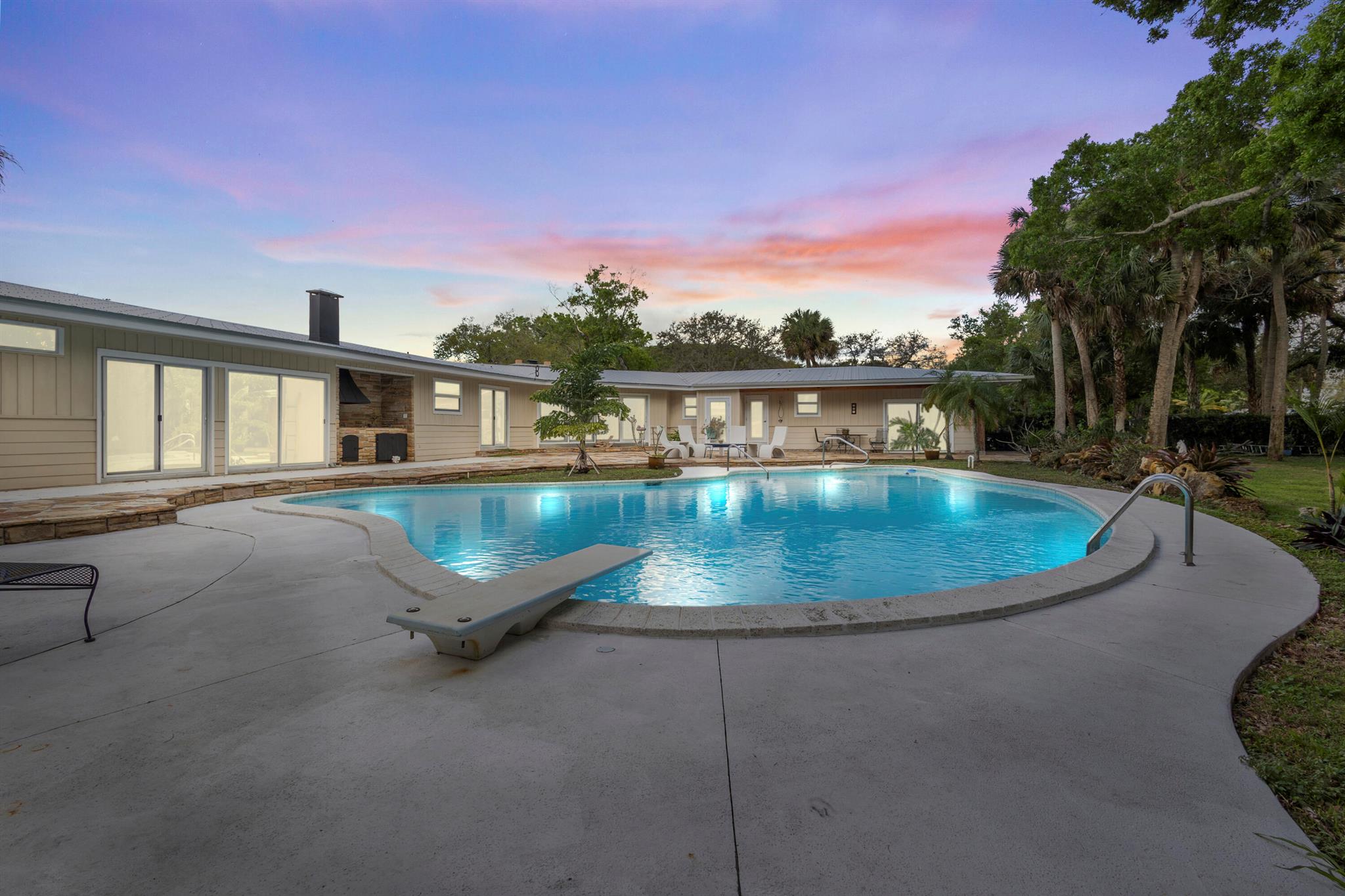 This stunning 5-bedroom, 4.5-bath pool home sits on 3/4 acre, beautifully landscaped corner lot, just 10 minutes from the beach and waterfront dining. Fully renovated, it blends modern updates with classic Florida charm. Inside, you'll find oak wood floors, terrazzo, and Brazilian red cherry block flooring, with cypress tongue-and-groove ceilings, crown molding, and recessed lighting. The updated kitchen features granite counters and stainless steel appliances. Enjoy a massive lagoon-style pool with a diving board, spa, and beach area, plus a summer kitchen and cabana bath. Highlights include impact glass windows, a metal roof, two new AC systems, a 3-car garage, two laundry rooms, a wood-burning fireplace, two new water heaters and a flagstone-paved patio. Don't miss this retreat!