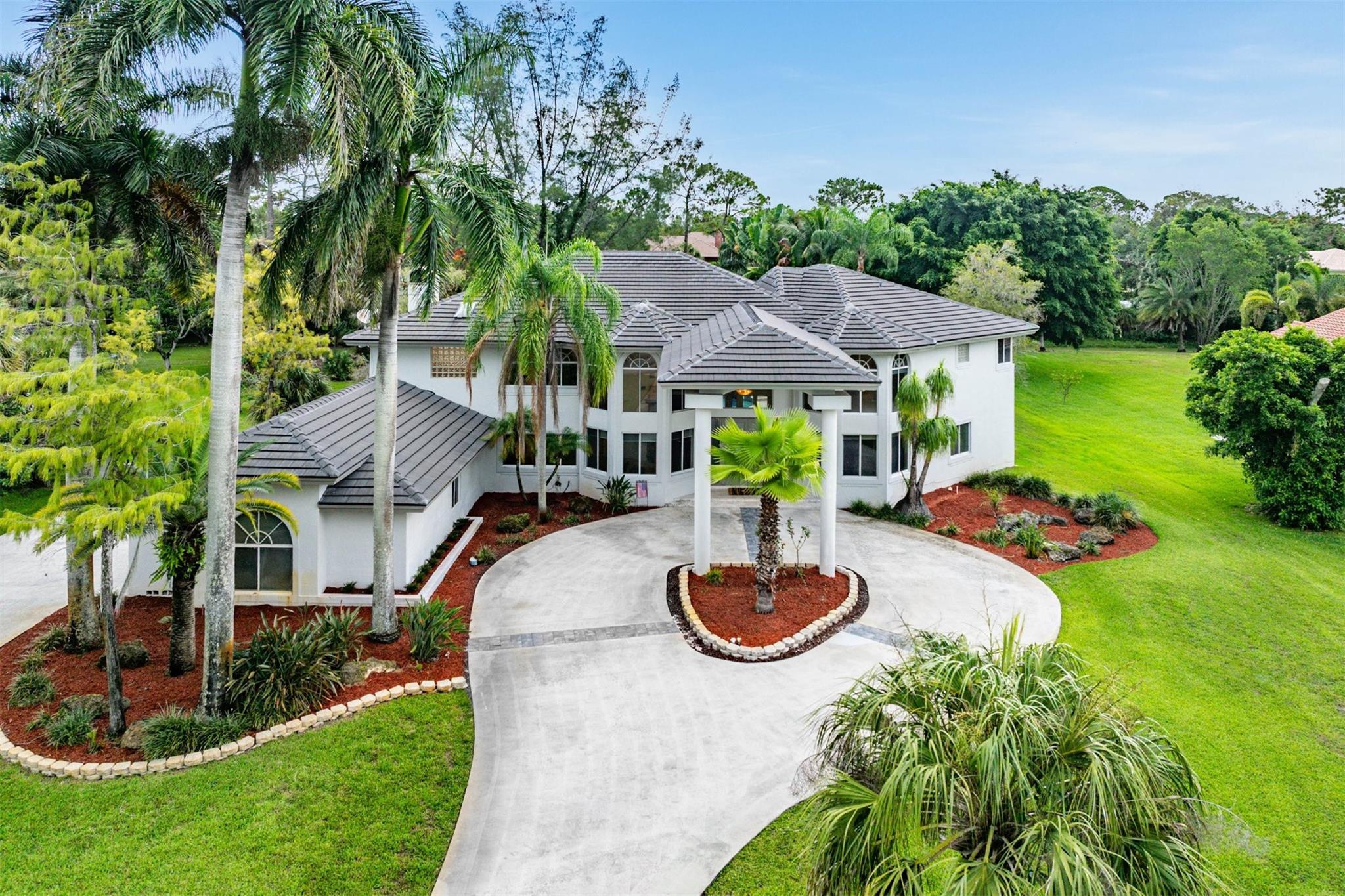 Beautifully Big! Impressive curb appeal with two long driveways, a porte cochere, sprawling lawn, & a 2020 flat tile roof. Inside, soaring two-story ceilings & walls of windows flood the home with natural light & tropical pool views. The stunning newer kitchen features sleek European-style cabinetry, quartz counters, Thermador appliances including a gas range, & glorious windows. The spacious primary suite offers a 2022 spa-inspired bath, office/den, sitting & dressing areas, a balcony over looking the grounds & an oversized closet. The backyard is a private oasis with a large pool, porch, serene outdoor living spaces & is perfect for enjoying family & friends. Other offerings: Fireplace, den, wine chiller, large secondary bedrooms with ensuite baths, bar, wood floors and so much more.