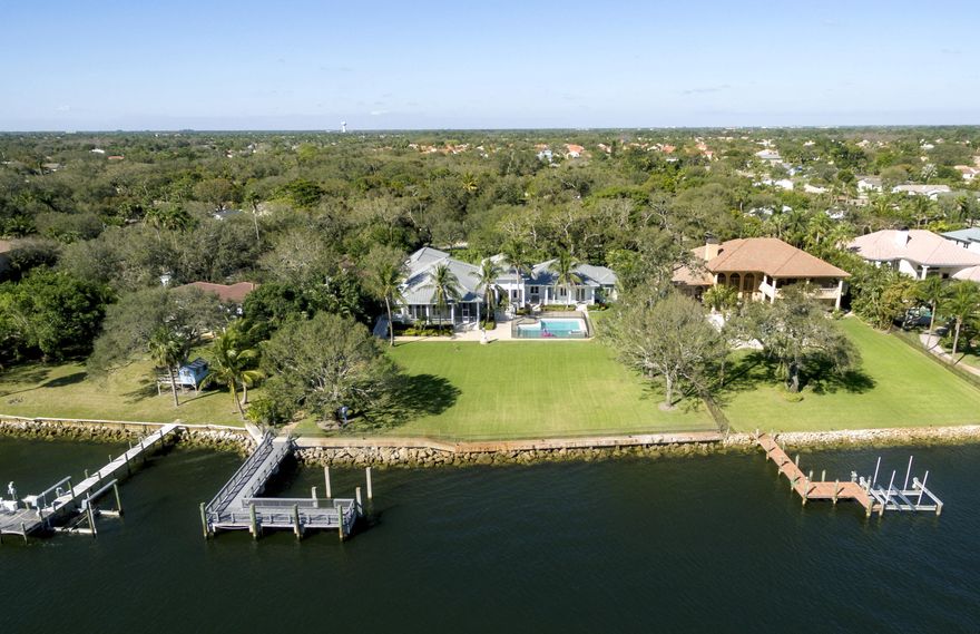 This custom built and impeccably designed estate home is on 1.13 acres located directly on the Intracoastal Waterway. The manicured front lawn features large Oak and Banyan trees and a 4 car garage with a Key West inspired metal roof. A large entrance Foyer has a vaulted ceiling and gas fireplace and is a perfect spot for your holiday decorations.  The water views from almost every room in the home are truly spectacular especially from the kitchen and family room which feature tall hurricane impact windows, high end appliances including a Wolf gas range (a high performance cooking range with precise control) a wine cooler with an ice maker and maximum cabinet space with additional large pantry space.  From the formal dining area are large water views looking out over the massive back yard. There is a large covered patio extending into the backyard and pool area that wraps around back of the home and large portions are screened which make a perfect outdoor dining area for entertaining your family and friends.  On the south side of the porch is a ramp for easy access to the yard and dock for those that need easier access than stairs.  The pool is large enough to entertain many guests and has a spa.   A large dock made with long lasting composite materials is supported with concrete pilings and concrete support pilings made for a lift are already in place and a concrete seawall with fence spans across the entire backyard.  Inside the home are 5 bedrooms which are split and feature 5 full bathrooms and an additional half bath.  The master bedroom has full backyard water views and a huge bathroom with a his and her walk in closet.  4 central AC units are in place to keep this home nice and cool all summer long and in the winter months many of the impact windows feature hardware that make it effortless to open and allow the easterly ocean breezes to sweep through all the rooms.  The flooring is mostly Brazilian Cherry hardwood with the bathrooms and large laundry (with 2 freezers and a sink) having clay tile. In case of foul weather and other unexpected outages a 45KW Gas generator is in place with 1000 lbs of propane to keep you up and running for many days at a time.  In the hallway on the south side of the home are 4 large closets for extra storage and this leads to the four car garage which has plenty of extra space for bicycles, holiday decorations and such.  All this is covered with metal roof which will protect this home completely for decades to come.