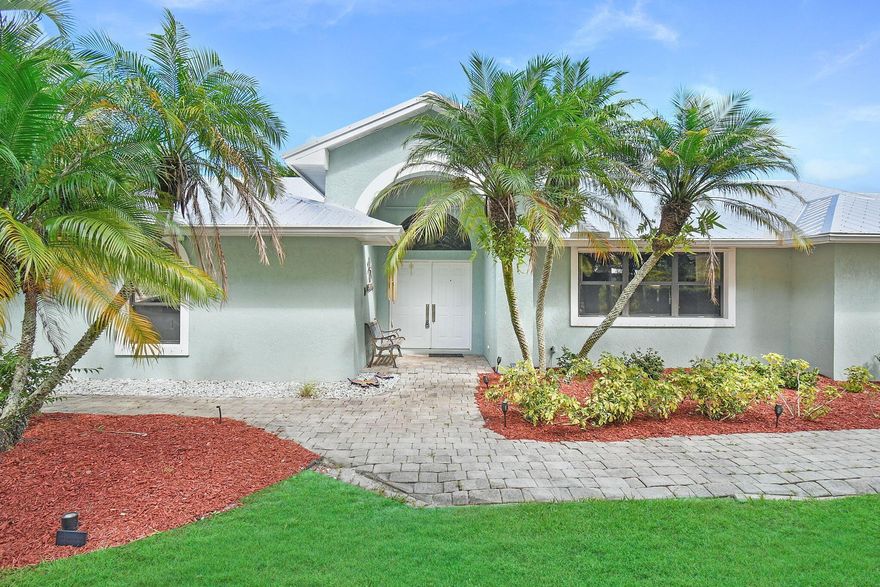 Some opportunities only knock once...don't miss your chance to own this charming 4-bedroom home nestled in the peaceful cul-de-sac of Magnolia Bluff in Palm City. This 4/2 split floor plan features a new metal roof, a cozy living area with surround sound media, stunning wood floors, security cameras and a renovated gourmet kitchen with granite, cabinets galore, two breakfast bars and an oversized pantry. Unwind on the screened patio while your furry friends enjoy the fenced-in astroturf dog run. The property includes two garages (one is HUGE), offering covered space for five cars and a workshop. Additional perks include a generator hookup, two driveways, and ample attic storage. With a top-rated school district, this property is ideal for families seeking luxury and location.