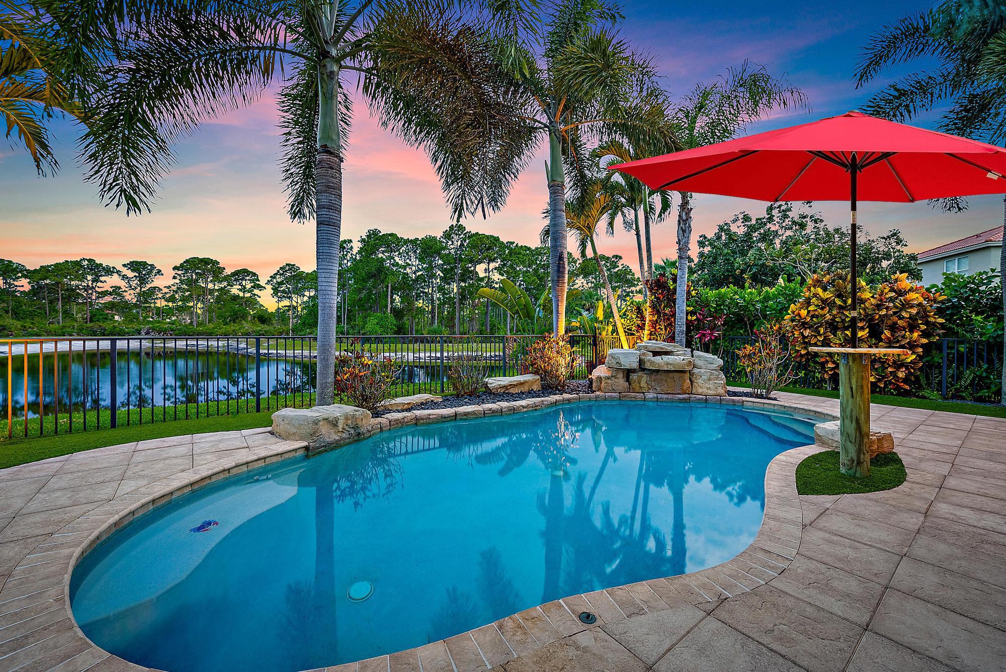 Experience LUXURY living in this stunning 4-bedroom, 3.5 bath pool home located in the sought-after Oaks of Hobe Sound. This beautifully designed lakefront residence offers the perfect combination of style, functionality, and peace of mind. Step inside to soaring 20-foot ceilings and an abundance of natural light. Features include a custom electric fireplace, wood-look porcelain tile throughout the main level, and IMPACT windows. The gourmet kitchen is complete with stainless appliances, double ovens, 42'' wood cabinetry, a center cook island, granite counters, and a picturesque window overlooking the pool and lake. The first floor primary suite is a true retreat, offering direct access through sliding doors to the pool, perfect for a peaceful morning dip or evening swim under the stars.