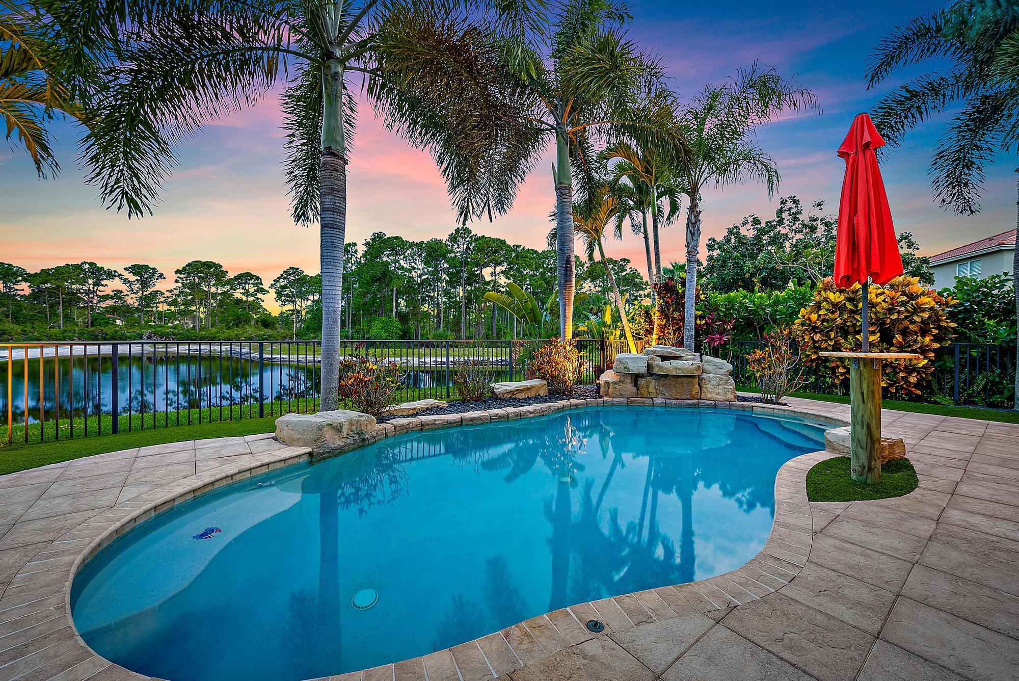 Experience LUXURY living in this stunning 4-bedroom, 3.5 bath pool home located in the sought-after Oaks of Hobe Sound. This beautifully designed lakefront residence offers the perfect combination of style, functionality, and peace of mind. Step inside to soaring 20-foot ceilings and an abundance of natural light. Features include a custom electric fireplace, wood-look porcelain tile throughout the main level, and IMPACT windows. The gourmet kitchen is complete with stainless appliances, double ovens, 42'' wood cabinetry, a center cook island, granite counters, and a picturesque window overlooking the pool and lake. The first floor primary suite is a true retreat, offering direct access through sliding doors to the pool, perfect for a peaceful morning dip or evening swim under the stars.