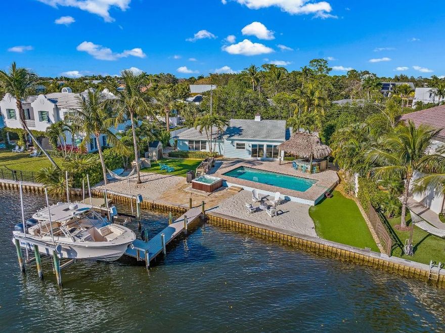 Welcome to this beautifully renovated waterfront retreat, where coastal elegance meets resort-style living. Step outside to an exceptional backyard designed for both entertaining and relaxation, featuring a spacious paver patio, heated saltwater pool, above-ground hot tub, and an expansive tiki hut with seating for 12 and a TV. Two sand lounge areas, a private dock with boat lift, and sweeping wide-water views of the Loxahatchee River complete this outdoor oasis.

The home greets you with a manicured lawn, circular driveway, and the privacy of a quiet, no-thru-traffic street. Inside, a sunlit foyer leads to luxury vinyl plank flooring throughout and an open-concept living space filled with natural light. Soaring ceilings and a striking wood beam add warmth and architectural character,