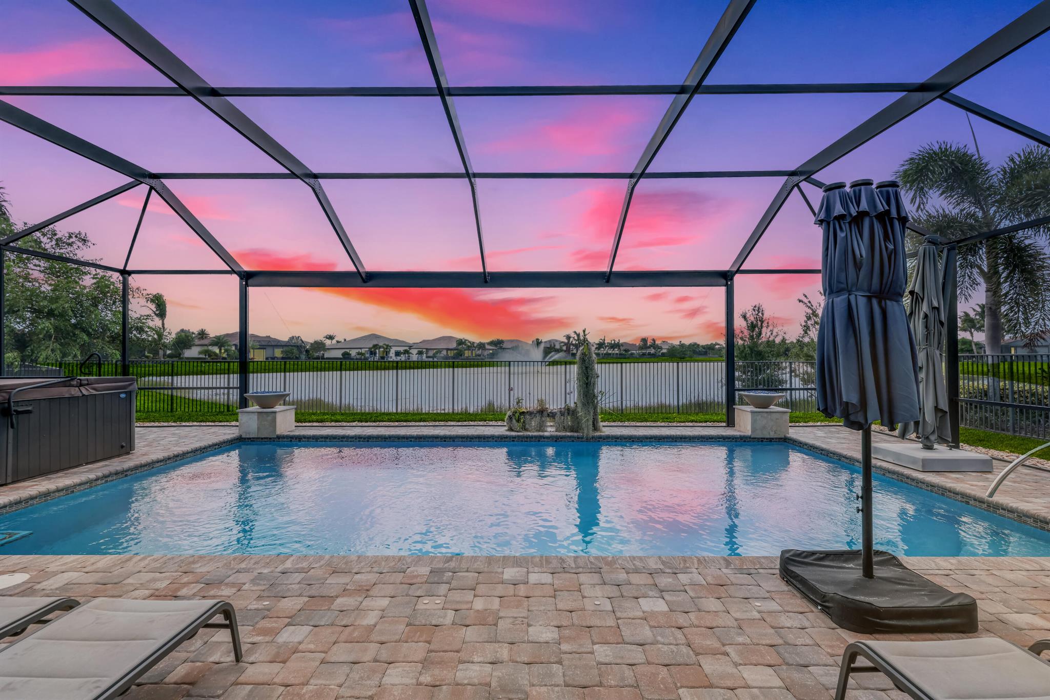 On one of the largest lots in Ancient Tree, this half-acre lakefront home offers wide fountain views and a backyard built for enjoyment. The saltwater heated pool, 6 1/2 feet deep, with fire bowls, hot tub, and panoramic screen enclosure, creates the perfect outdoor retreat. Entertain with ease on the patio featuring a summer kitchen with grill, fridge, ice machine, and trash. Inside, the custom kitchen includes 42'' upper cabinets, upgraded quartz, built-in pet bowls, and premium appliances: Fulgor range with gas burners and double electric ovens, wall oven, microwave, and pot filler. The open great room has coffered ceilings, while the primary suite offers generous closet space. Natural gas serves the dryer, water heater, grill, and burners. Oversized 3-car garage plus golf cart space.