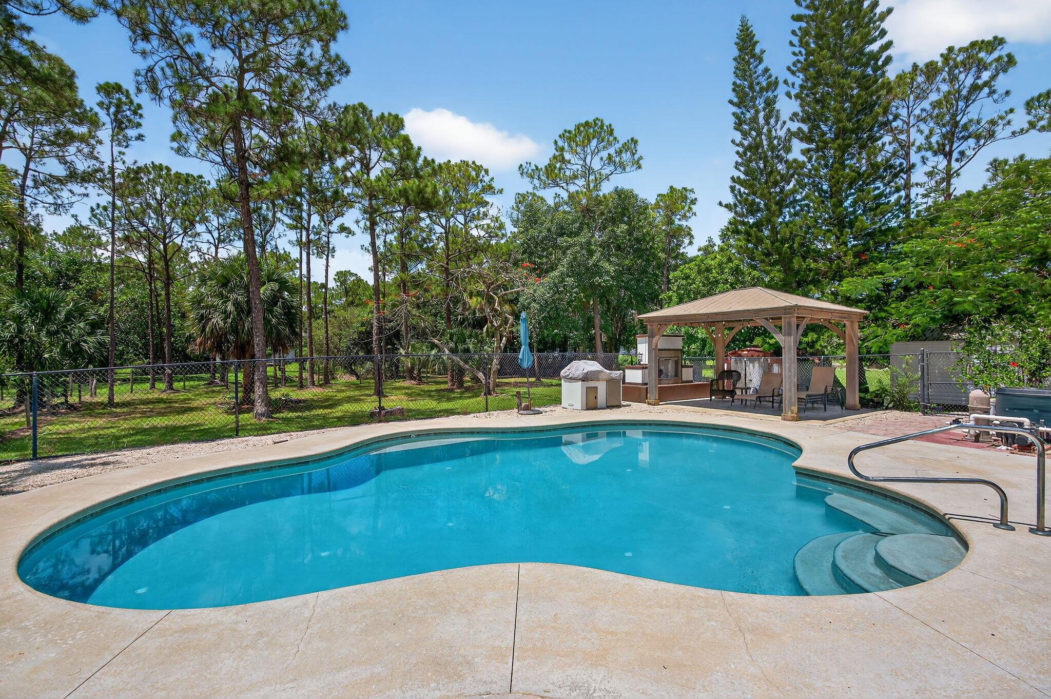 Beautiful, private, 4/3 with a pool, located in the highly sought-after Jupiter Farms neighborhood. Home features open split floor plan that's very spacious with lots of bright natural light, wood burning fireplace, new LED lighting and fans throughout entire house, high vaulted smooth modern finish ceilings. No popcorn ceilings, laundry inside, new flooring throughout entire house. All bathrooms are remodeled. Screened pool area leads to a back yard oasis that features a huge free formed pool with LED, new pool pump heater and chiller for year-round use. Outdoor gas fireplace. New water heater, 50-amp RV/boat outlet, new house well, A/C has UV light sanitizer, stainless steel appliances, double gate entries and 7'' gutters, updated landscaping, new water system and more......