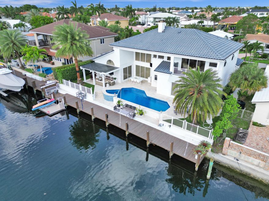 Stunning coastal contemporary, 4 bedroom, 4.5 bathroom home with 90 feet of water frontage. This beautifully finished property offers 3 bedroom suites on the ground floor, a stunning chef's kitchen overlooking the tranquil pool and backyard as well as a spacious 2 car garage with EV ready electric panel. The fireplace, elegant formal living and dining room are inviting yet impressive with atrium ceilings. The second floor is exclusively reserved for the primary, with an oversized bedroom suite, two luxurious bathrooms, two walk-in closets as well as a private balcony to enjoy stunning sunsets or a quiet morning coffee. The entire home has brand new hurricane impact windows, doors and shutters throughout. A beautiful, glistening pool, the hot tub, gazebo, summer kitchen and bar area create the perfect ambiance for outdoor entertaining. The home has a full service dock with water and 50 amp electric as well as a floating dock available for all your water toys. The property is conveniently located on a wide canal, just minutes from the Hillsboro Inlet, no fixed bridges. The home's elegant furniture and furnishings are available for sale as well.