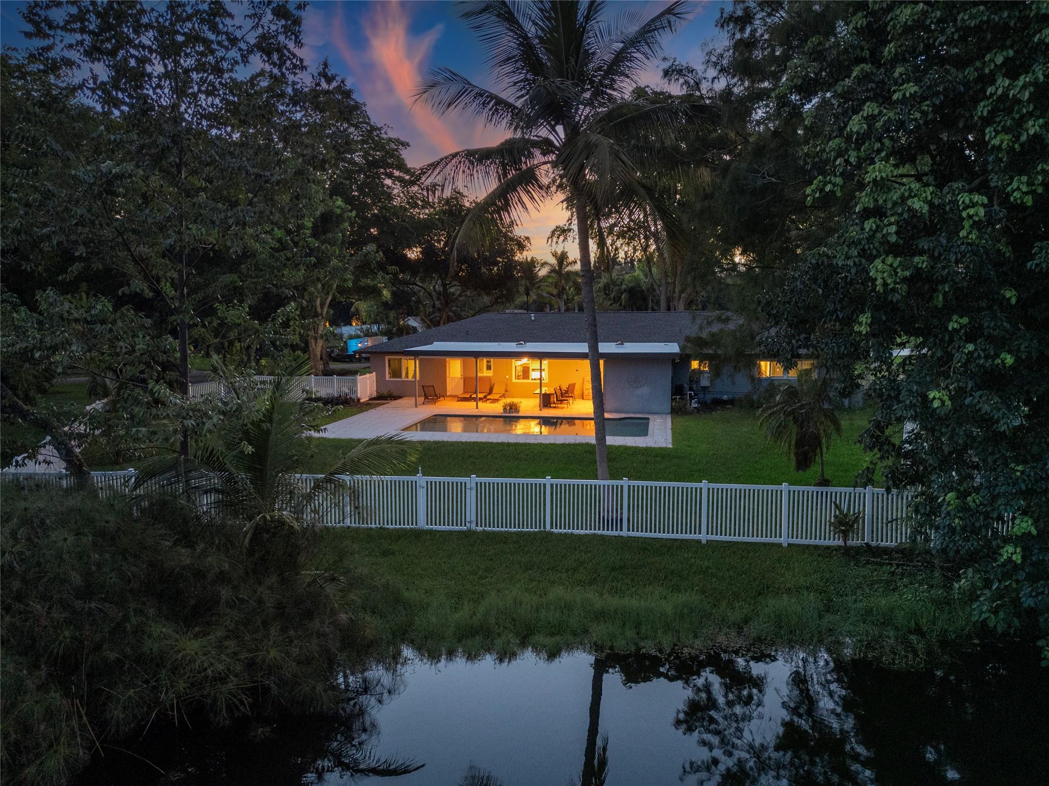 Tucked at the end of a double cul-de-sac in Davie’s Prestigious Hiatus Isles, this one-story retreat blends privacy and lifestyle. Wake up to shimmering lake views and birdsong, spend afternoons by the oversized pool or casting into a fish-filled pond, and gather in the evenings by a cozy fireplace. Sunlight fills bay-windowed living and dining rooms, while the eat-in kitchen perfectly frames the water. Sliding doors open to a covered patio for alfresco dining and sunset views, with room to add your own dock. In a serene, non-HOA enclave near top schools, every arrival feels like coming home. This is an opportunity to step into this lifestyle with ease.