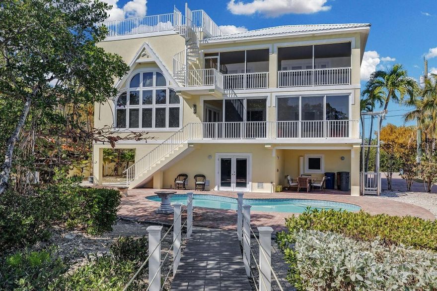 A rare estate package opportunity in the gated community of Stirrup Key, this four-story Luxury Custom residence is offered with a separate vacant lot with its own Parcel ID, a transferable building right, and a deeded boat slip in the community marina. Together, these features provide flexibility for future expansion, an additional residence, or long-term value in one of Marathon's most established neighborhoods. The home offers elevated water views, water access, and a layout designed for both everyday living and entertaining. The ground level features a three-car garage, generous storage, and direct access to the pool, creating easy indoor-outdoor living. The second floor serves as the main living level with two bedrooms, two full baths, a full kitchen, and open living and dining areas that extend onto a large screened lanai, ideal for relaxed gatherings and evening breezes. The third floor offers a private primary suite, sitting area or fourth bedroom, with bar/kitchenette and fireplace. Primary suite bath offers spa-style features, and an expansive lanai with elevated views. A spiral staircase leads to the fourth-floor widow's walk, finished with travertine flooring and a water hookup. From here, panoramic views stretch across Marathon and toward the Gulf, offering a peaceful setting for sunrise and sunset. A private nature path winds through preserved surroundings and leads to a Gulf-front observation dock, ideal for wildlife viewing and enjoying the natural setting. Additional features include a lift to the second floor for added convenience. Located behind the airport with easy access to shopping, dining, and daily necessities, this property offers a rare combination of space, privacy, boating access via a deeded marina slip, and future development potential in the Florida Keys. Schedule a private showing to experience the space, views,& the value of the additional lot, transferable building right, and deeded marina slip in person. B&BATVAI